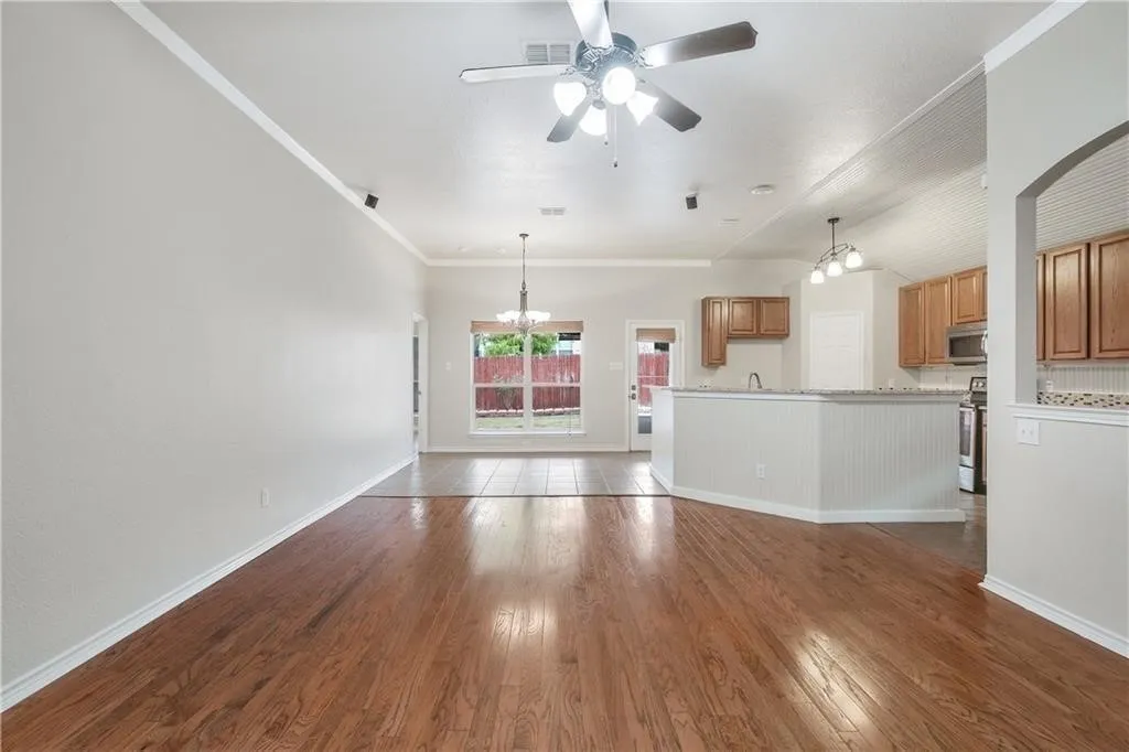 Spacious open-concept living area showcasing rich wood-finish flooring, white shiplap wainscoting, and abundant natural light from multi-pane glass doors