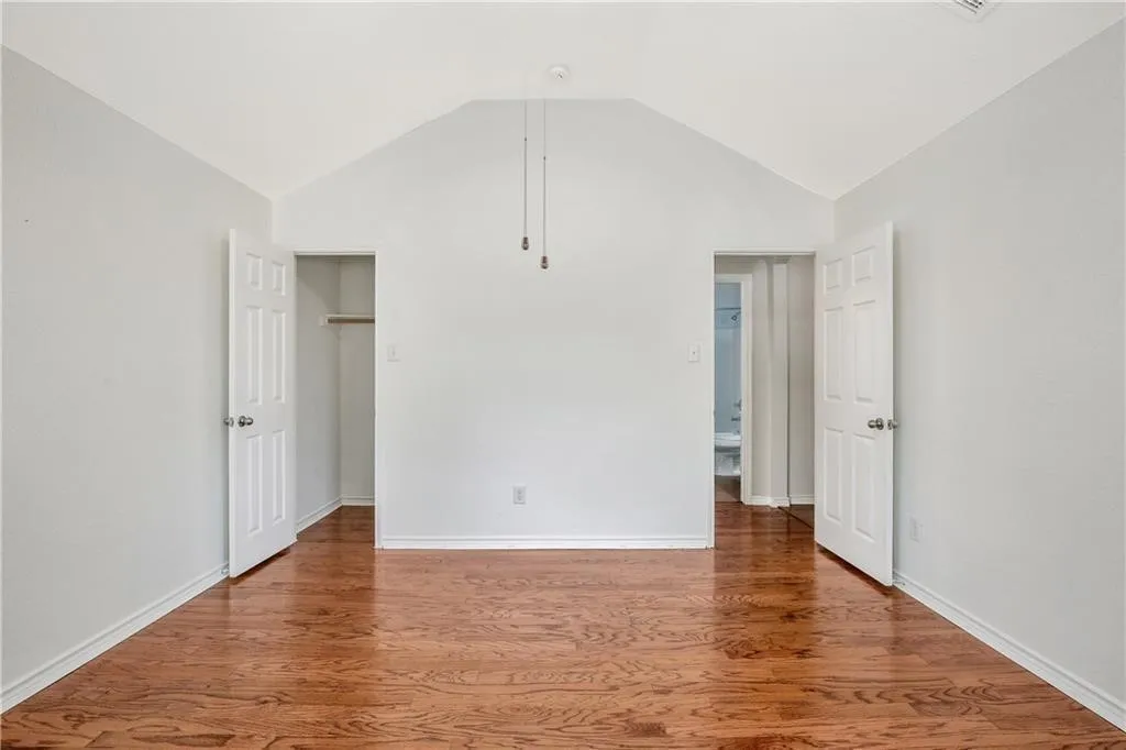 Spacious primary suite featuring soaring vaulted ceilings, hardwood flooring throughout, and dual walk-in closets with custom shelving