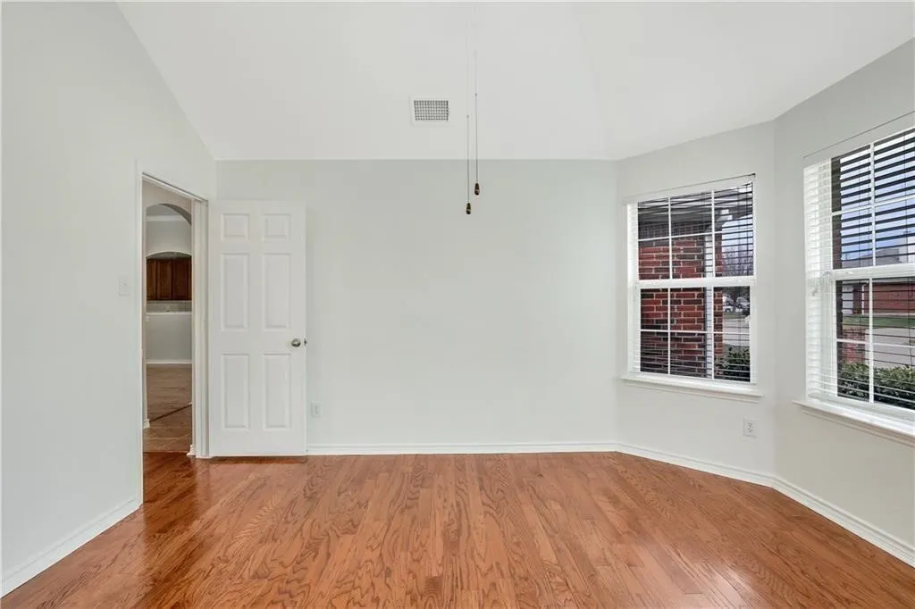 Vaulted ceiling with a flush-mounted light fixture, wood-finish flooring, and multiple windows with horizontal blinds