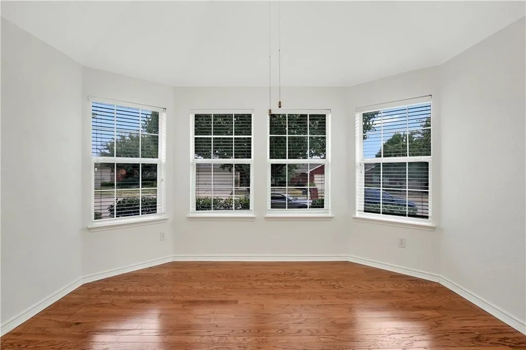 Bright corner room featuring four large double-hung windows with horizontal blinds, gleaming wood-finish flooring, and pristine white walls with recessed lighting
