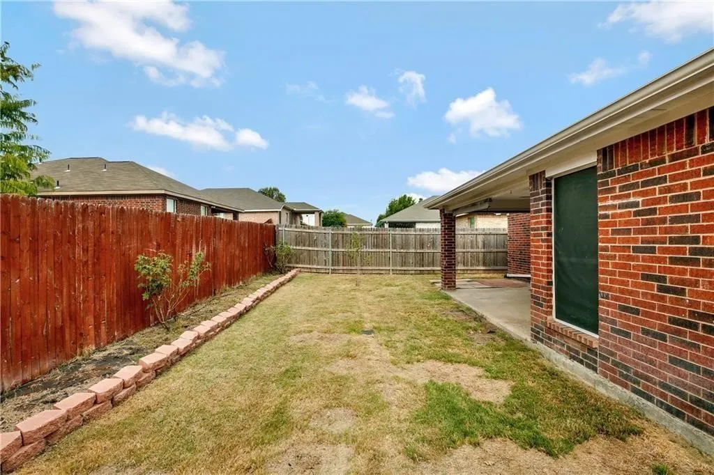 Spacious backyard with mature lawn, wood-finish fencing, and brick exterior home featuring a covered patio area and green entry door