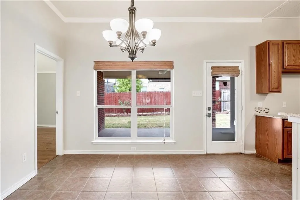 Bright, open kitchen and dining area featuring tile flooring, abundant natural light from dual glass doors and transom windows, brushed nickel chandelier, and wood-finish cabinetry with integrated appliances