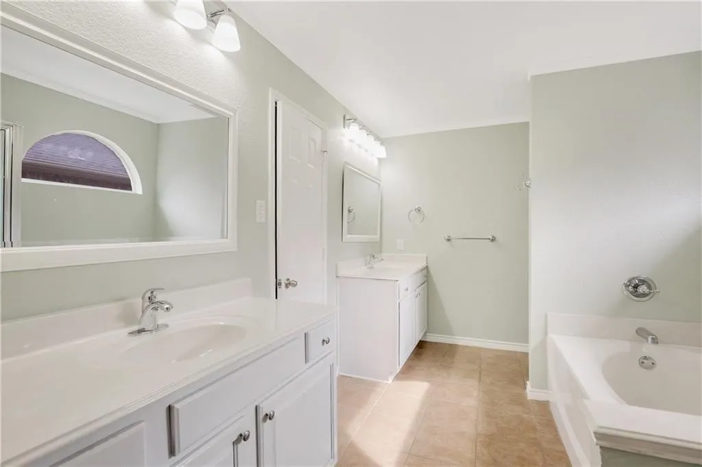 Dual vanity sinks, integrated bathtub, tiled flooring, and chrome fixtures