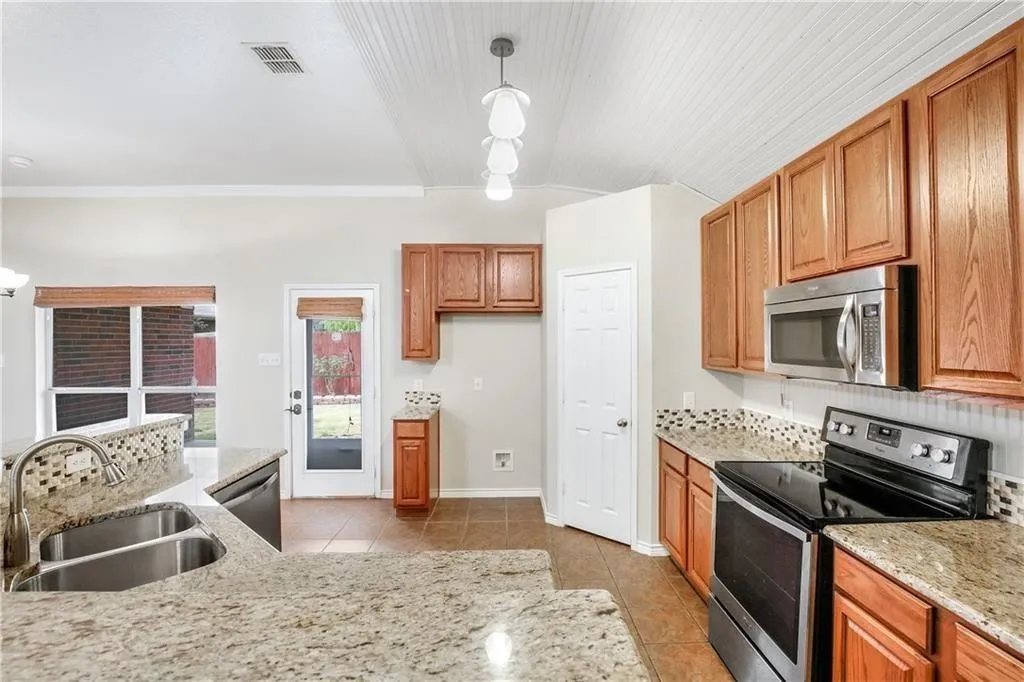 Spacious kitchen featuring warm wood cabinetry, speckled stone countertops, stainless steel appliances including a double oven, and an undermount sink with abundant counter workspace