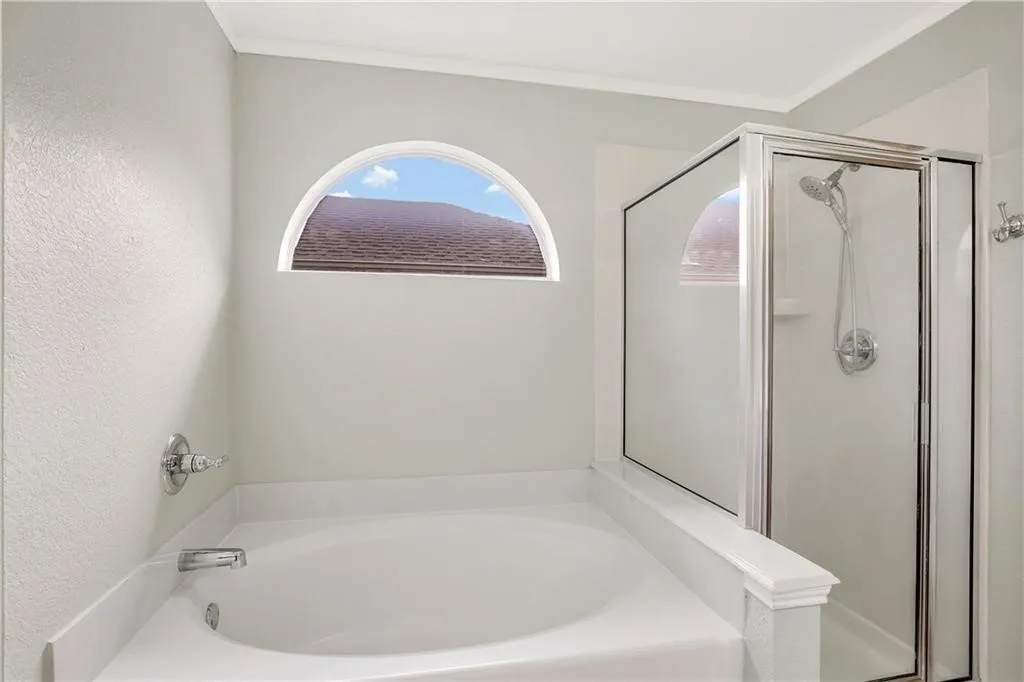 Soaking tub with a polished chrome faucet, an arched window, and a separate glass-enclosed shower with a handheld showerhead