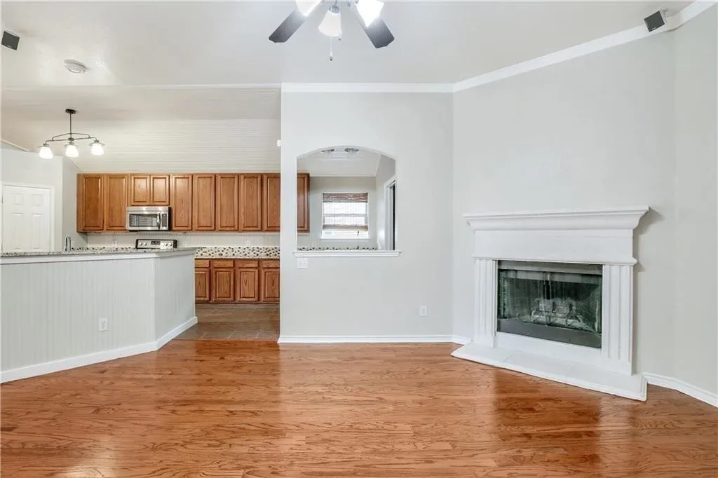 Wood-finish flooring throughout, white fireplace with hearth, vaulted ceilings, ceiling fan with integrated lighting, and kitchen featuring wood cabinetry