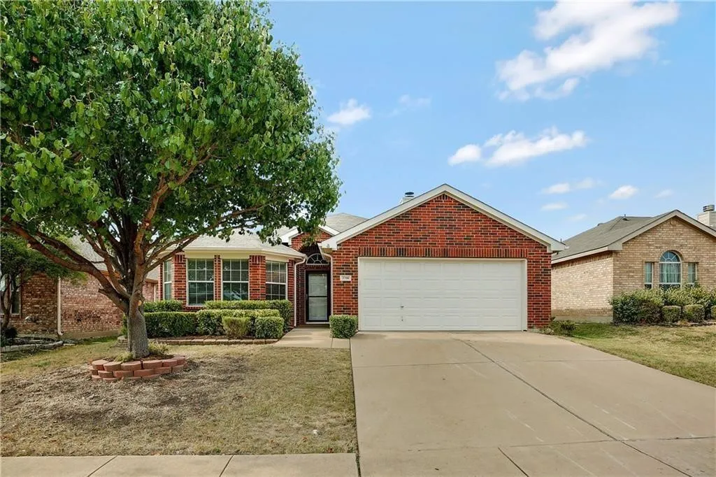 Red brick exterior with a two-car garage, mature front yard tree, bay window, and concrete driveway