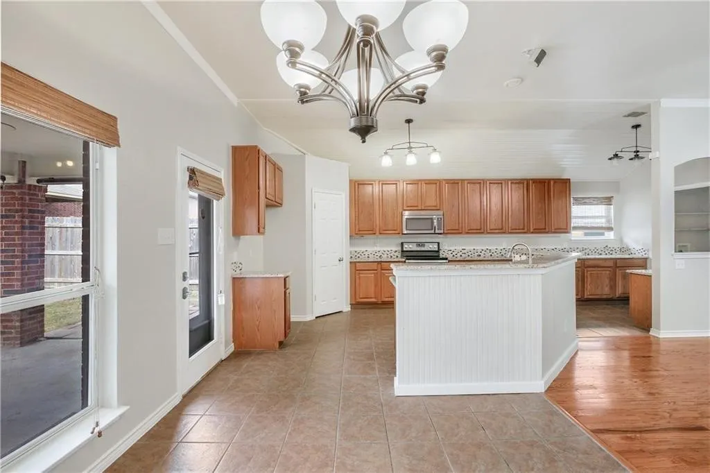 Spacious kitchen featuring wood cabinetry, stainless steel appliances, granite countertops, and a large central island with white paneling
