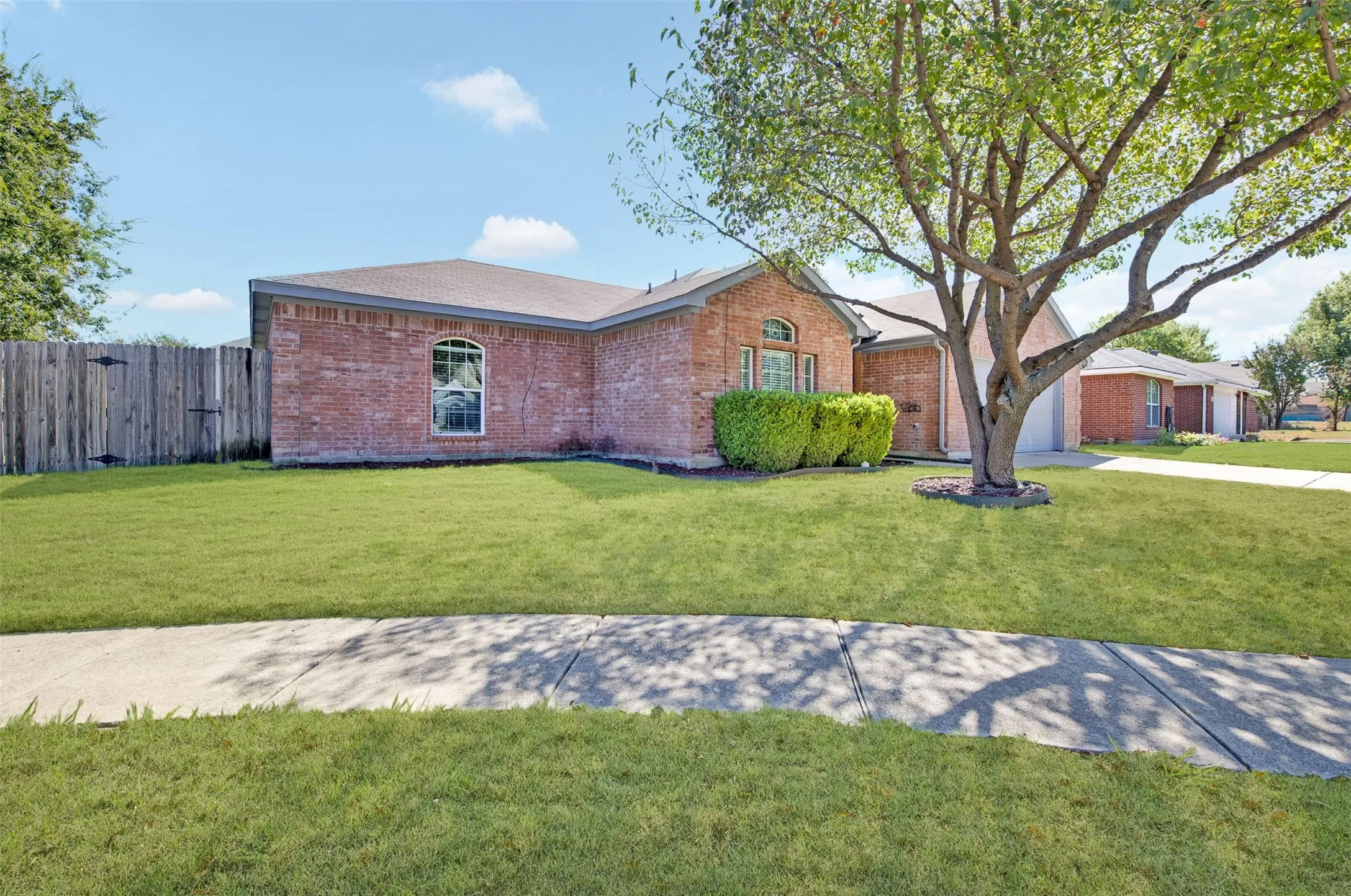 Brick exterior with an arched windows, a mature tree, and a concrete sidewalk