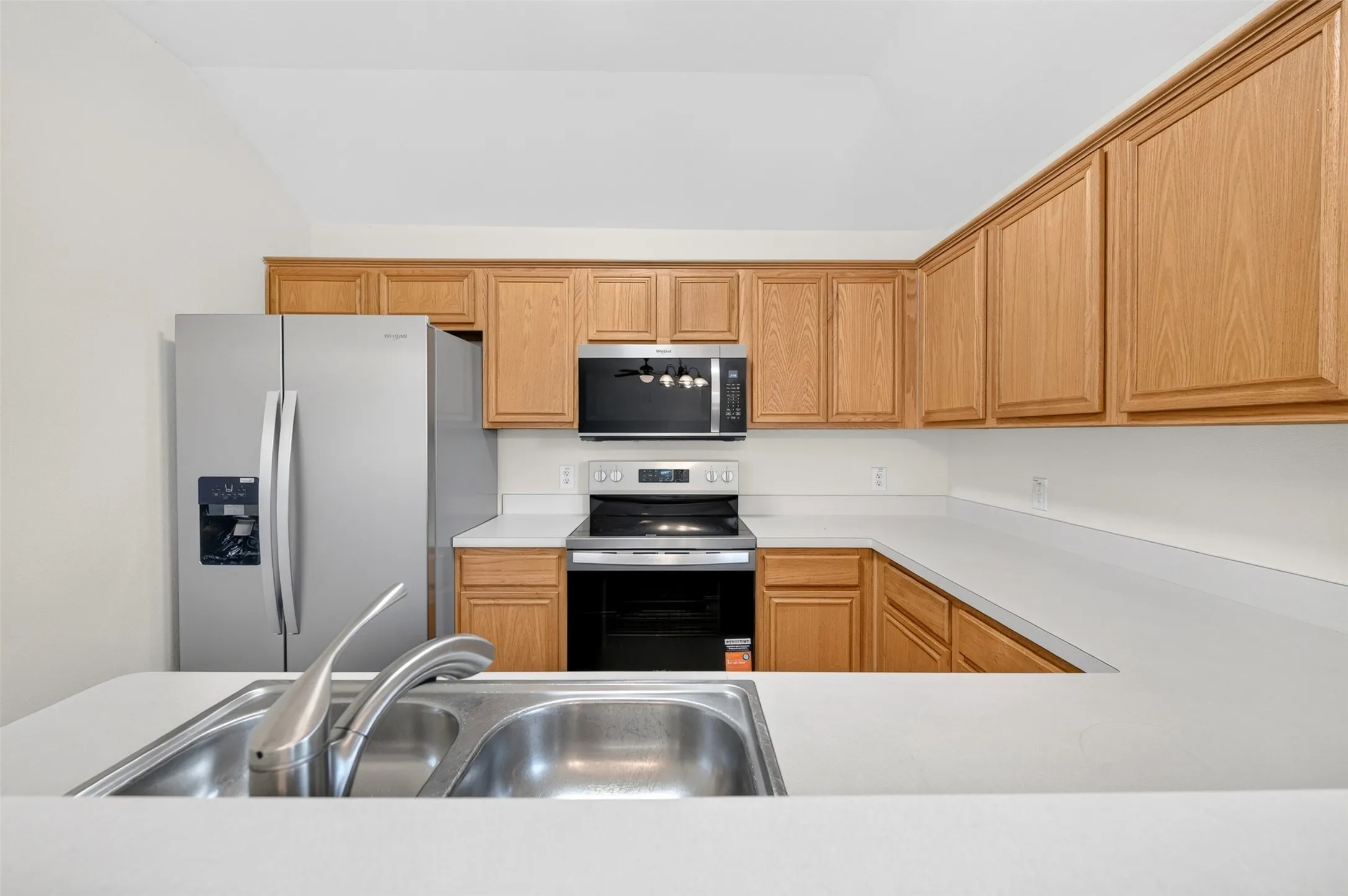 Kitchen featuring light wood cabinetry, a stainless steel double basin sink with a brushed nickel faucet, light-colored countertops, and new stainless steel appliances