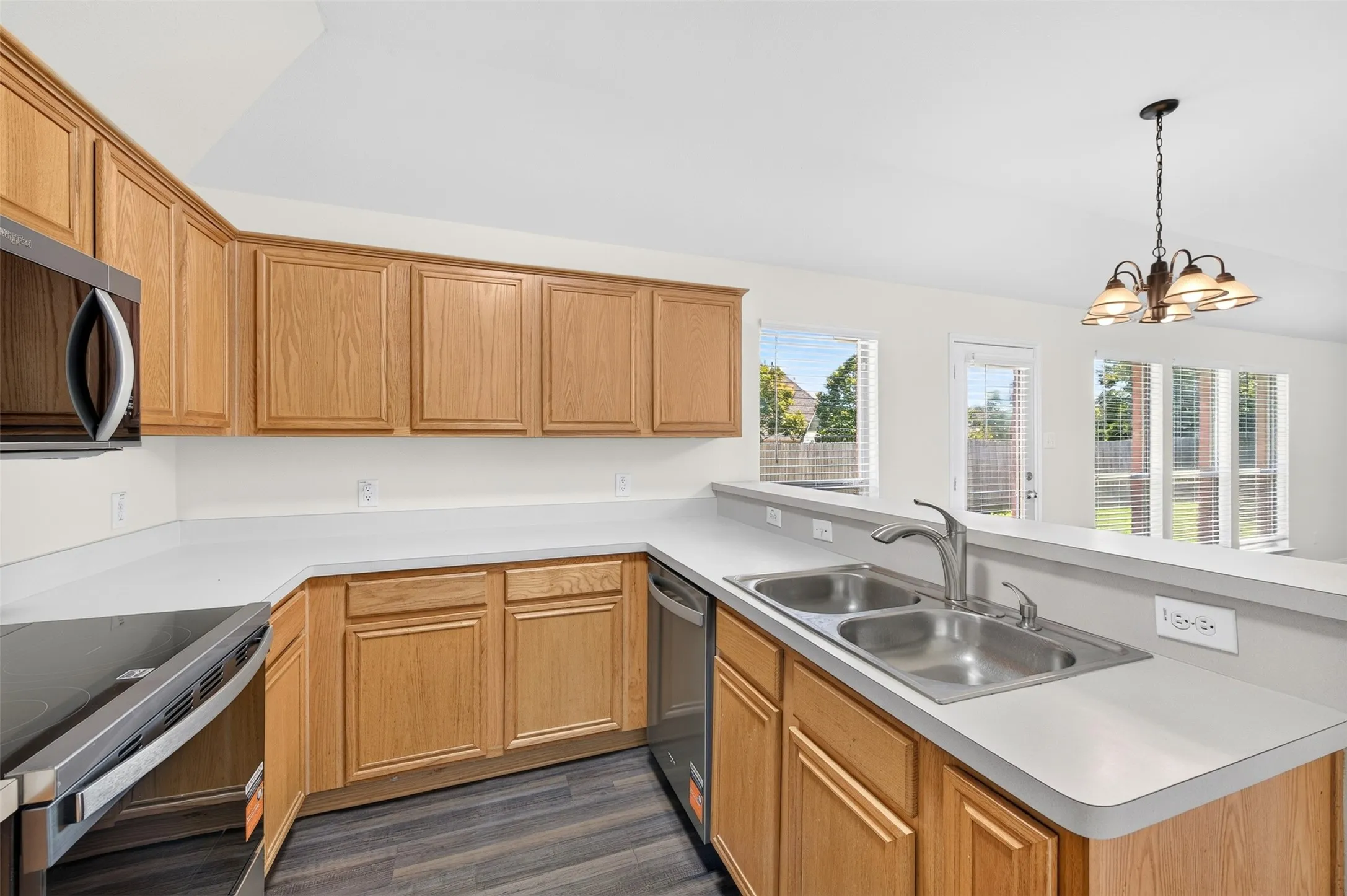 U-shaped kitchen with light wood cabinetry, light countertops, stainless steel sink, appliances and LVP flooring