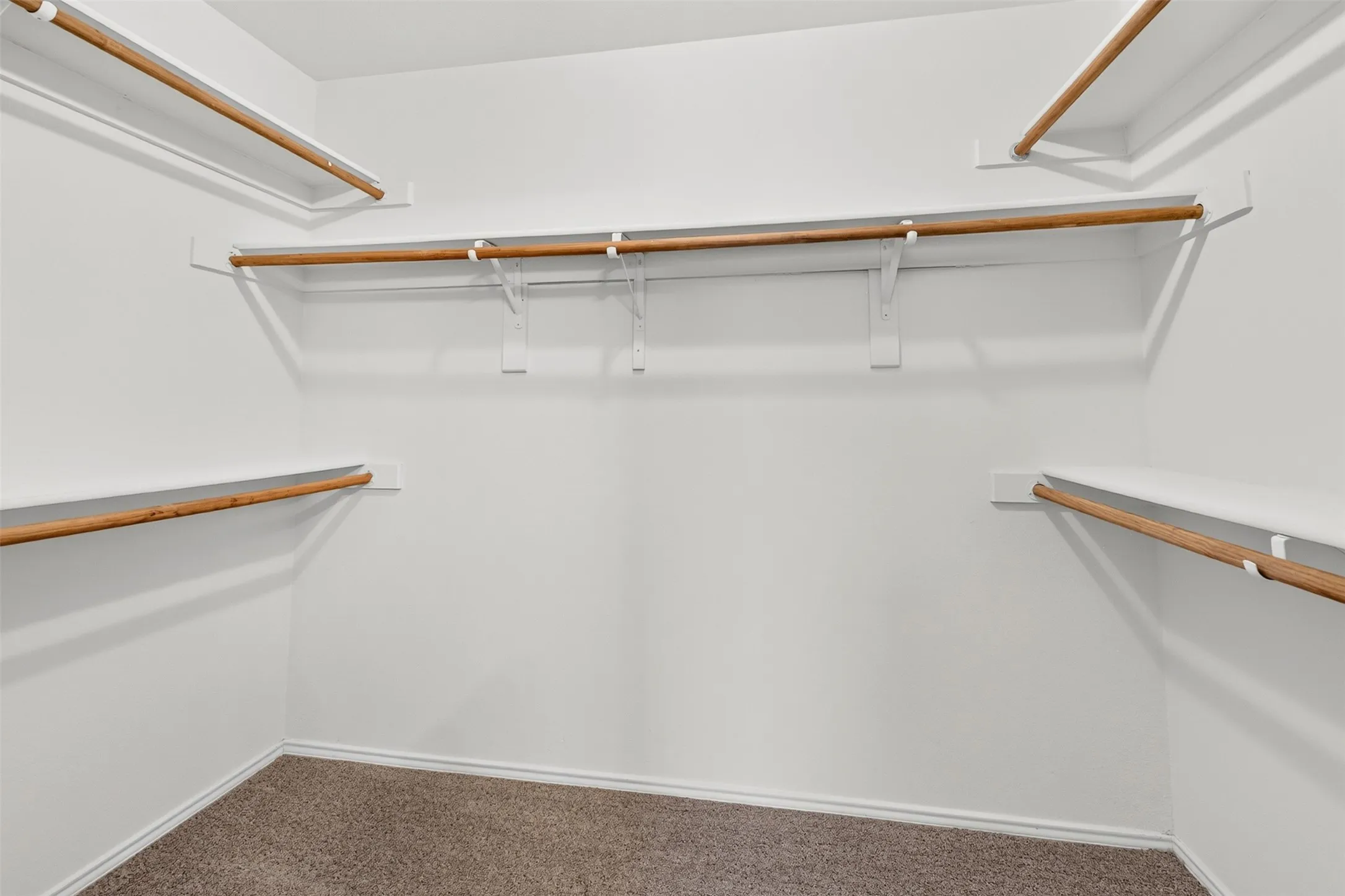 Spacious closet with multiple shelving levels and hanging rods, complemented by soft carpet flooring
