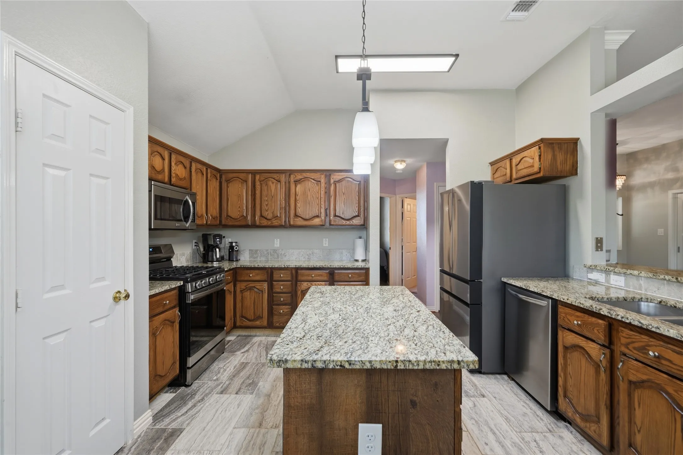 Kitchen featuring wood cabinetry, light-toned granite countertops, stainless steel appliances, and wood-finish flooring
