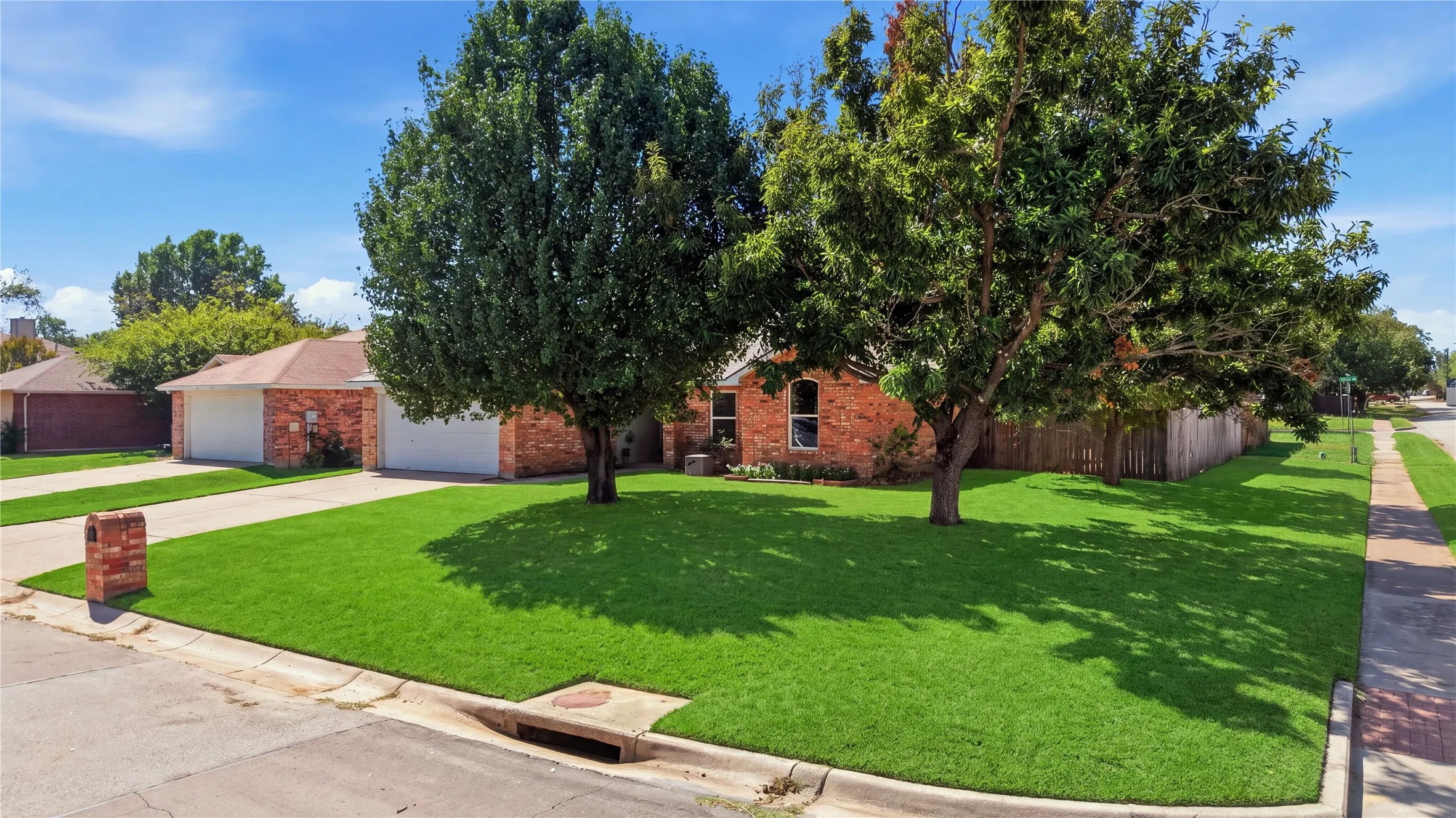 Brick exterior with an attached two-car garage, mature front yard trees, and a concrete driveway