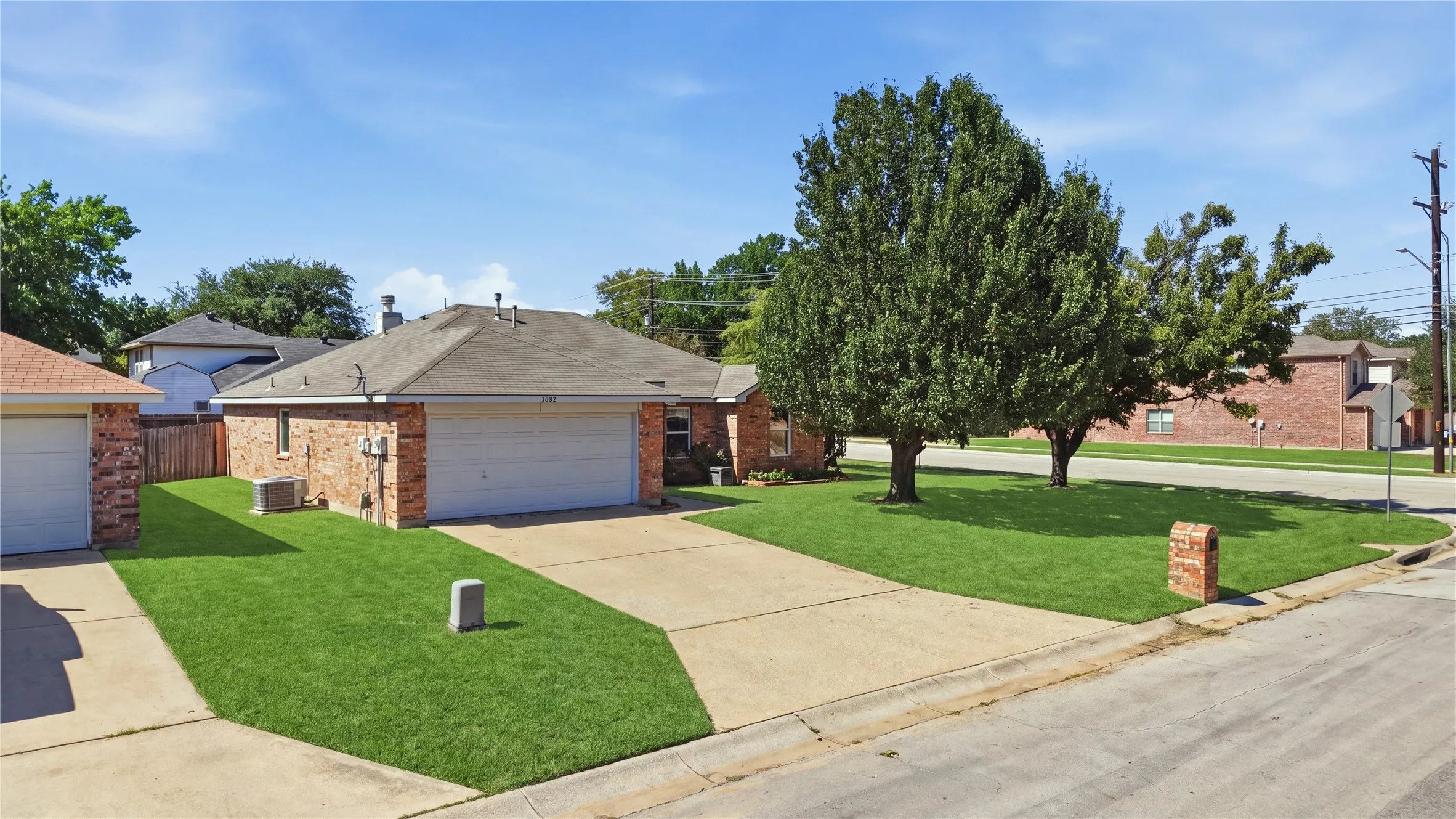 Brick exterior with a gabled roofline, front-facing garage, concrete driveway, and mature landscaping