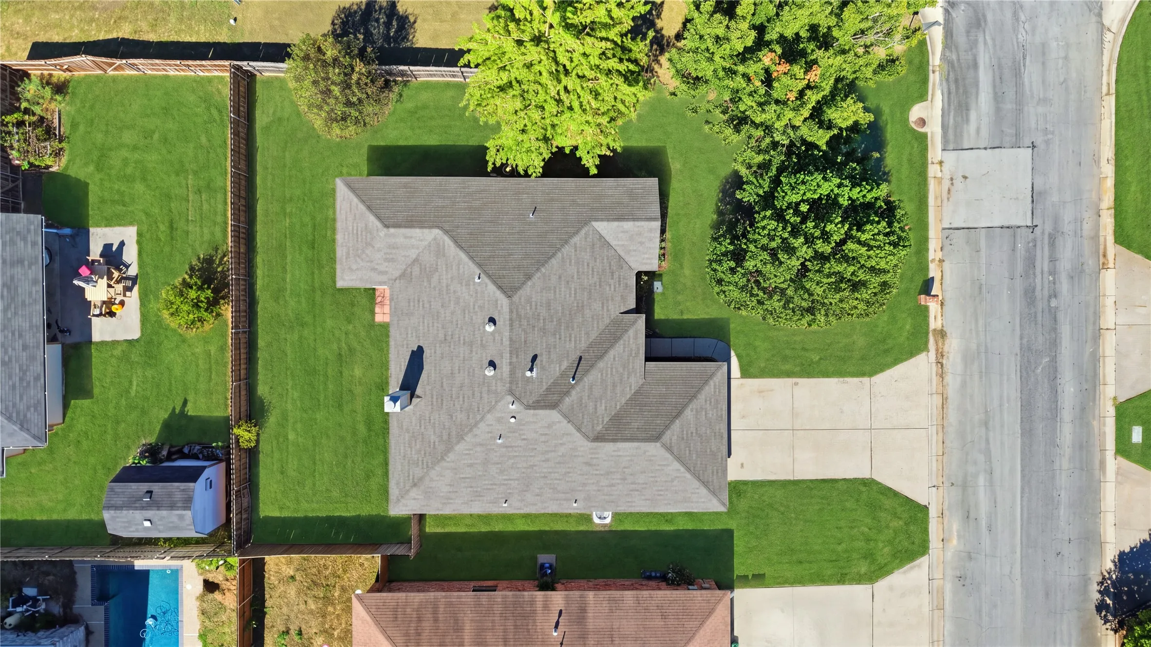 Gabled roofline, concrete driveway, front yard with mature trees, fenced backyard with manicured lawn, and a storage shed