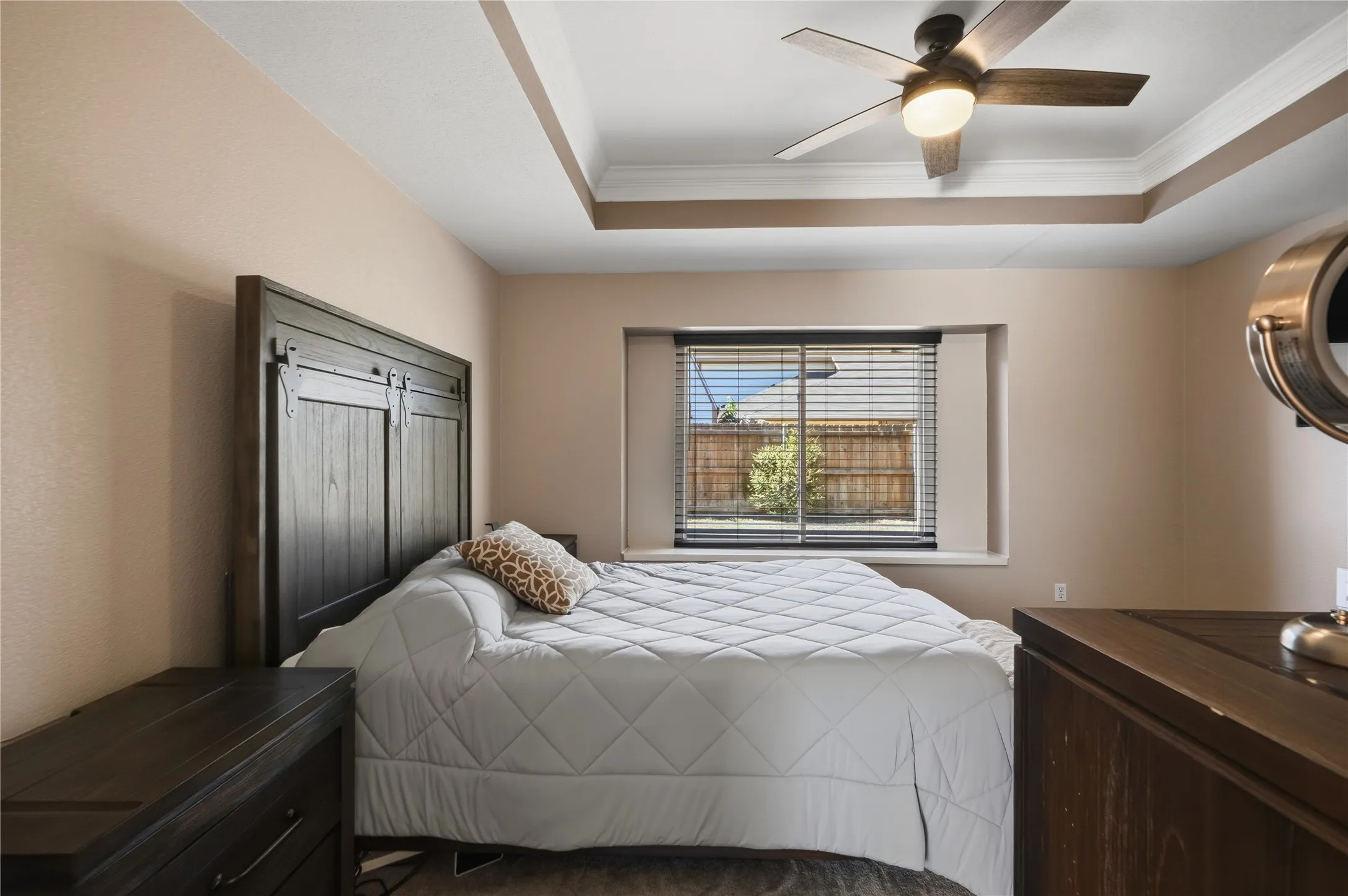 Tray ceiling with crown molding, ceiling fan with integrated lighting, window with blinds, and wood-finish flooring