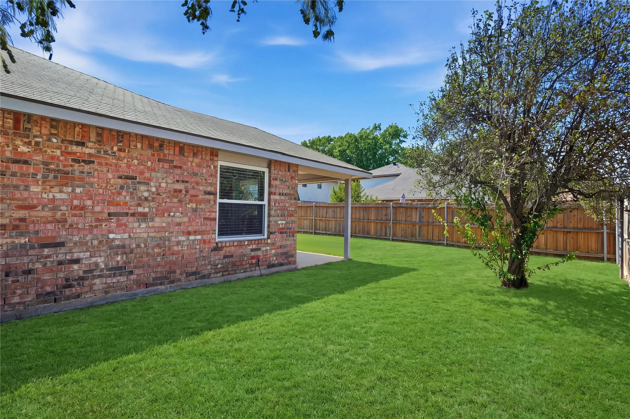 Expansive backyard with a manicured lawn, brick exterior, and a privacy fence