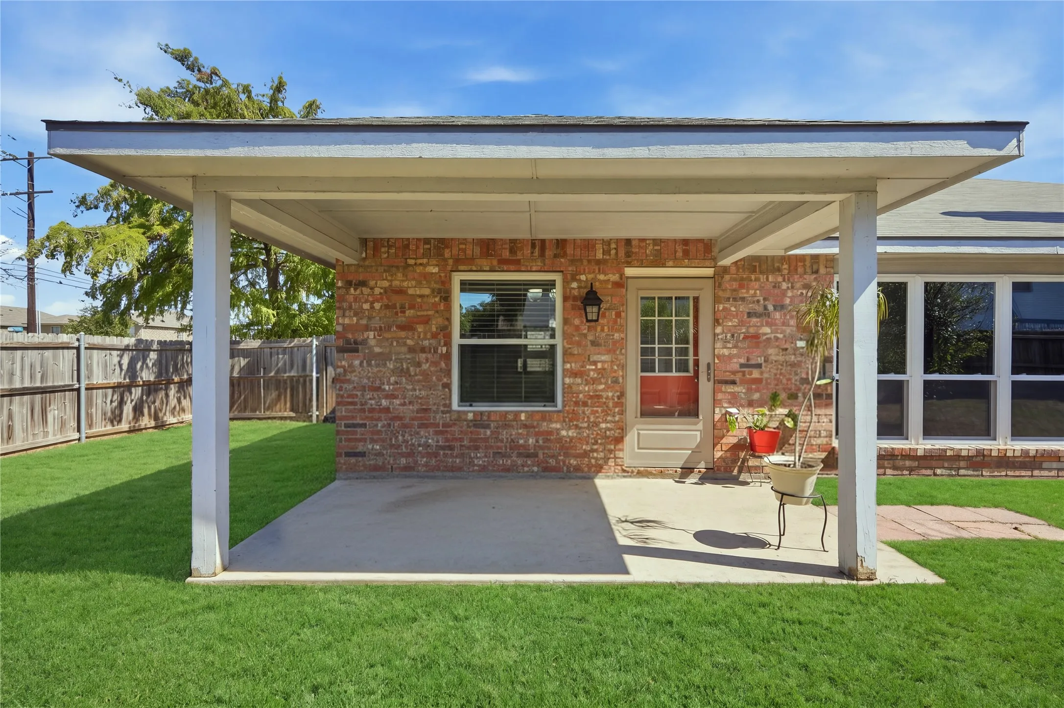 Expansive backyard featuring a covered patio, brick exterior, wood fence, and abundant natural lighting