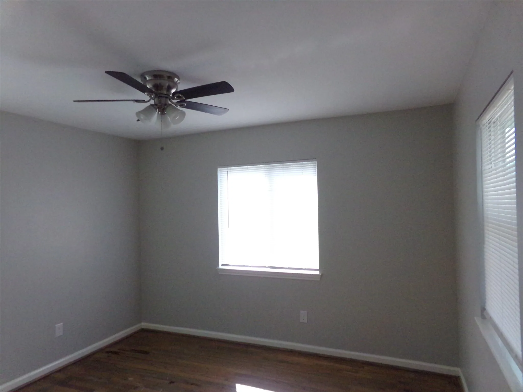 Recessed ceiling with an attached ceiling fan, wood-finish flooring, and multiple windows with blinds