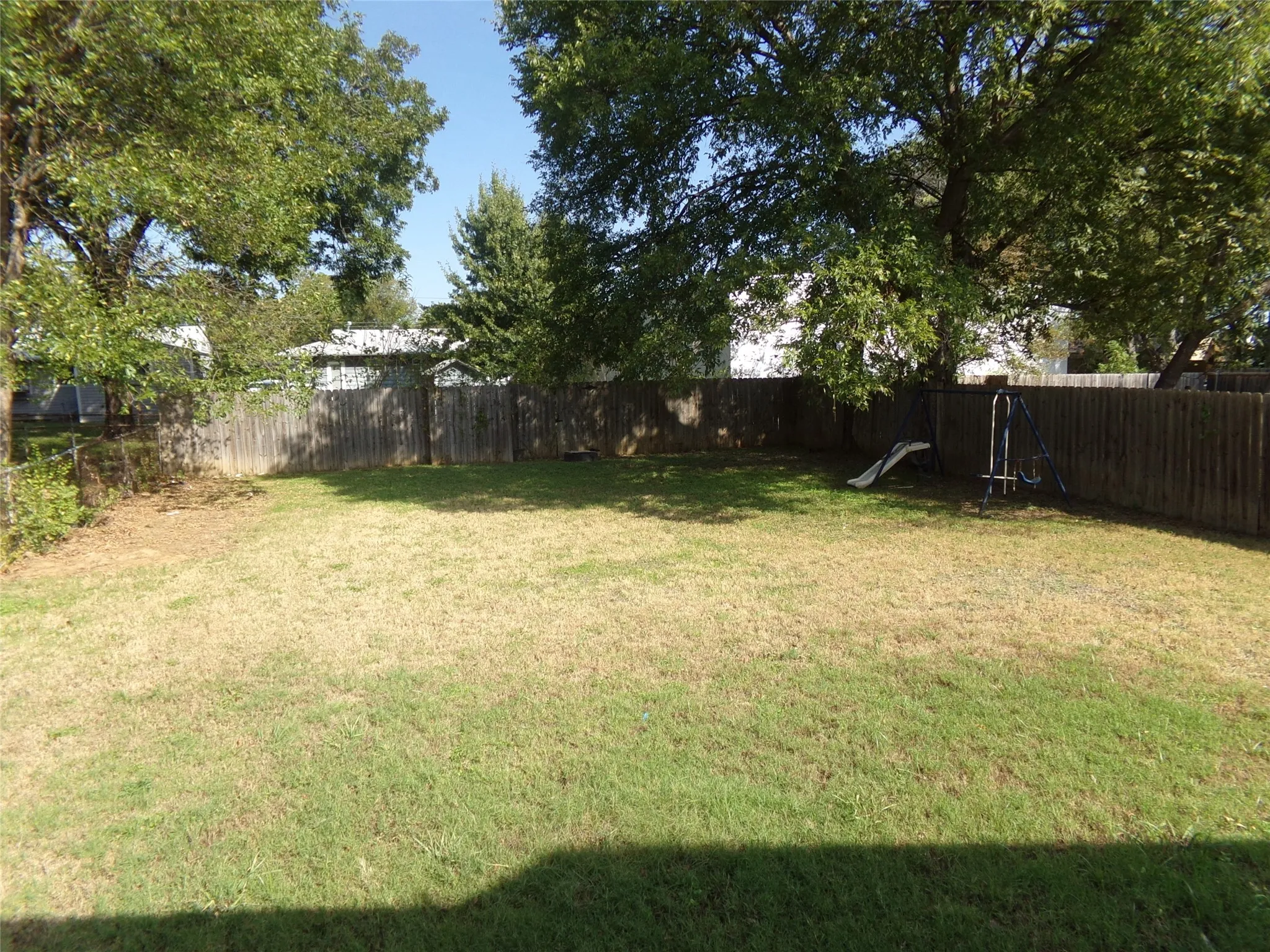 Expansive grassy yard with mature trees and a privacy fence