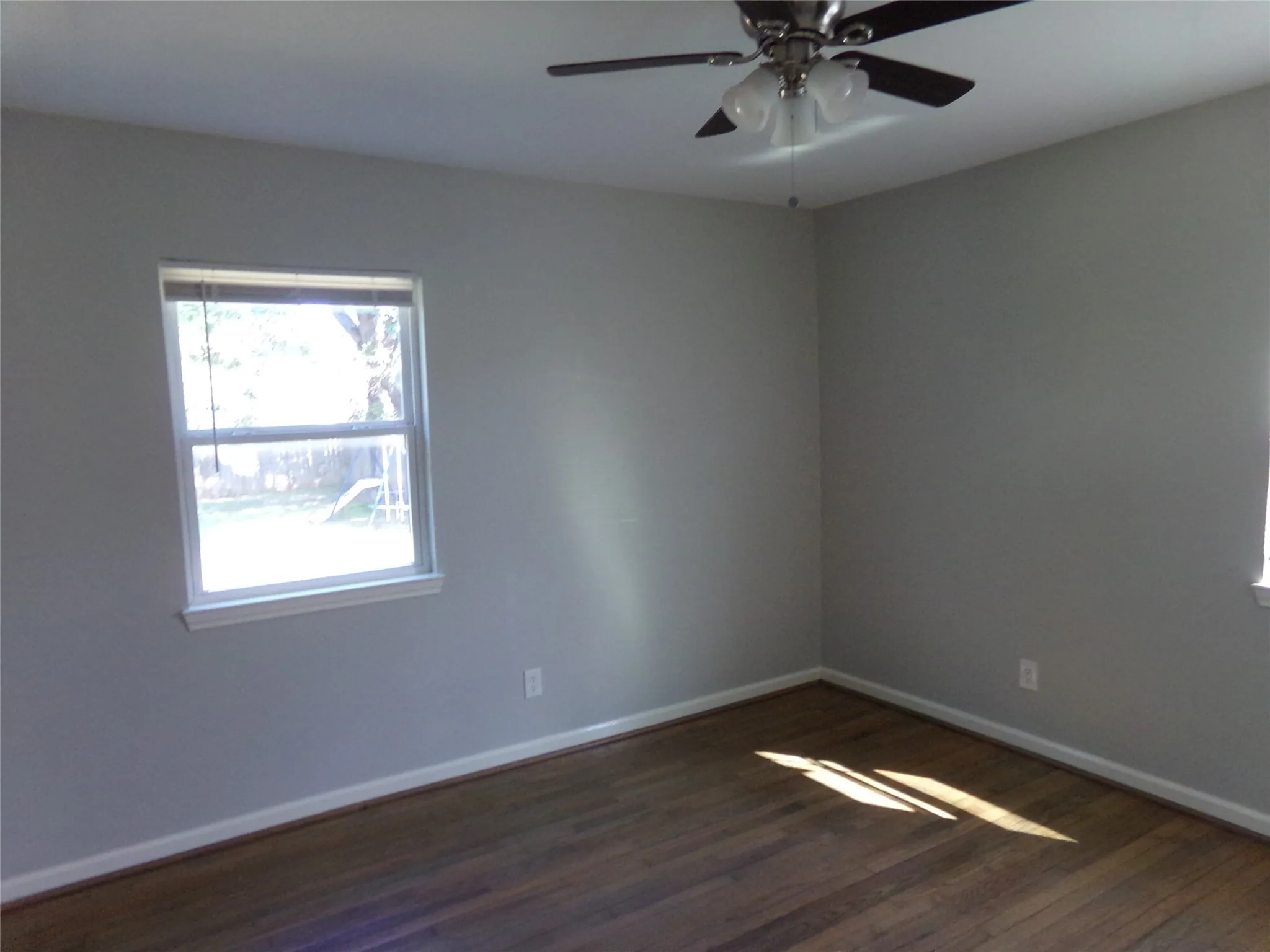 Wood-finish flooring, light grey wall paint, and a ceiling fan with integrated lighting