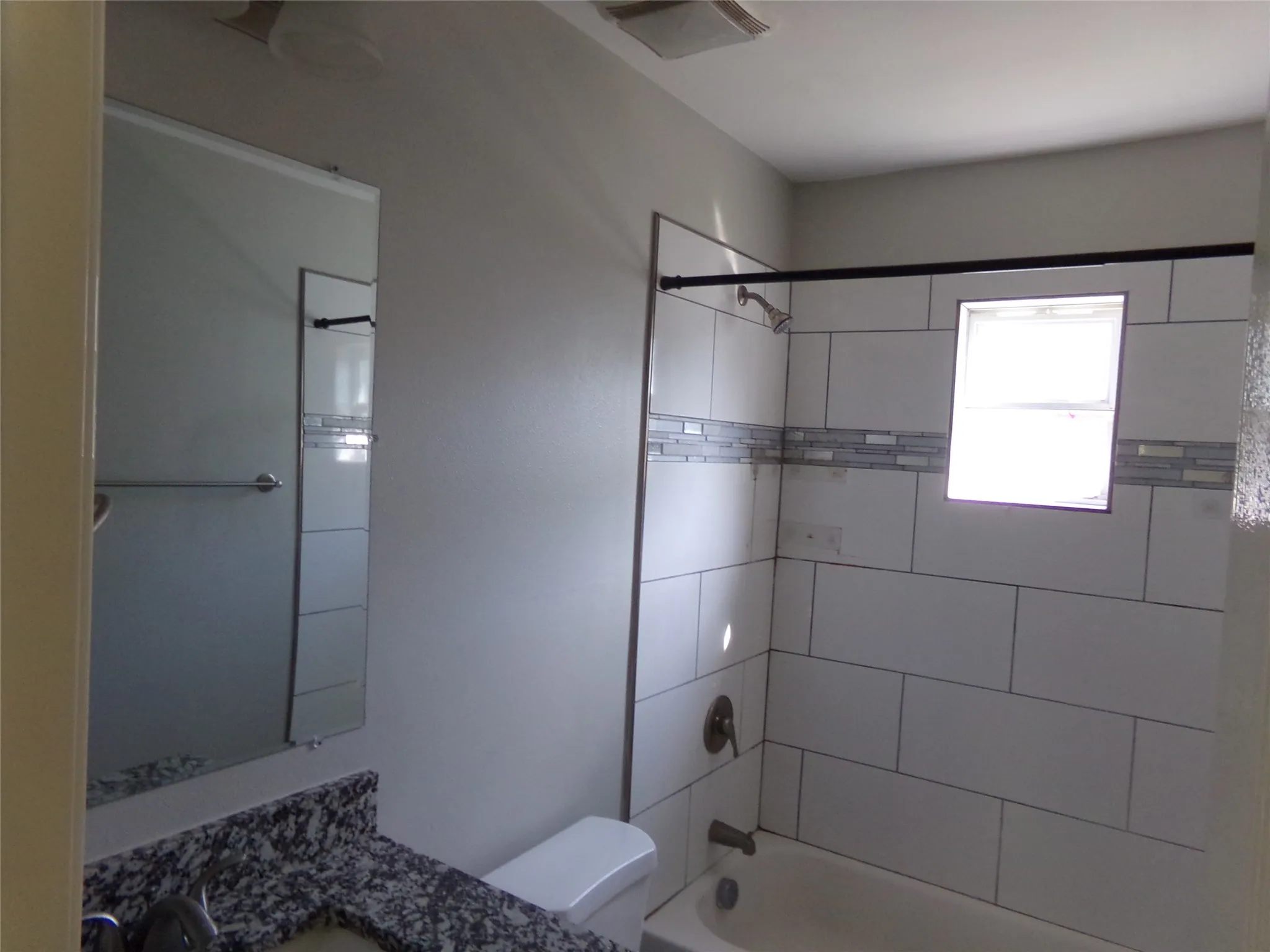 Bathroom featuring a white subway tile shower, decorative mosaic tile accent band, a built-in bathtub, a window within the shower, and a vanity with a stone-finish countertop