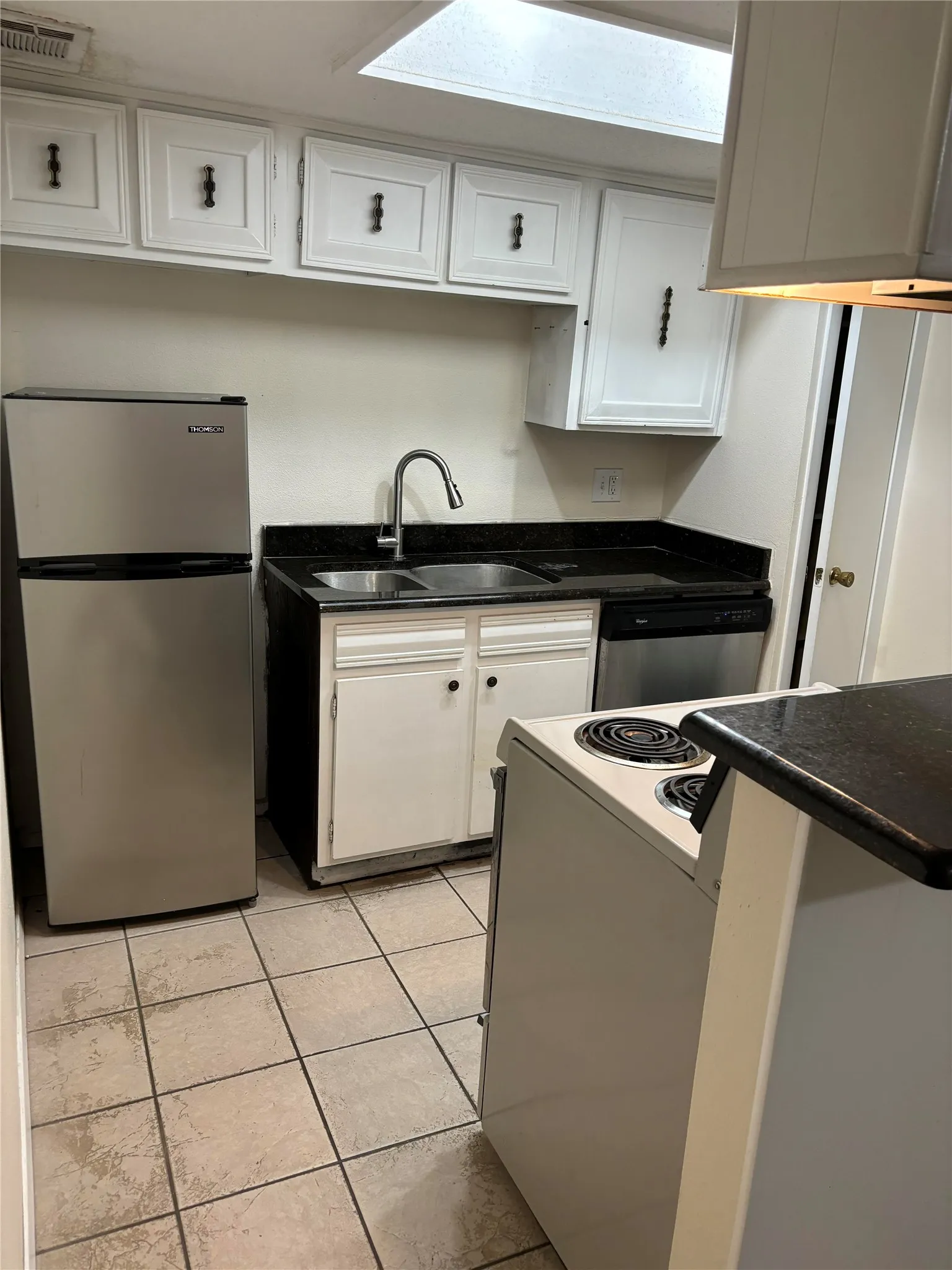Kitchen with stainless steel appliances, exhaust hood, white cabinetry, sink, and light tile floors
