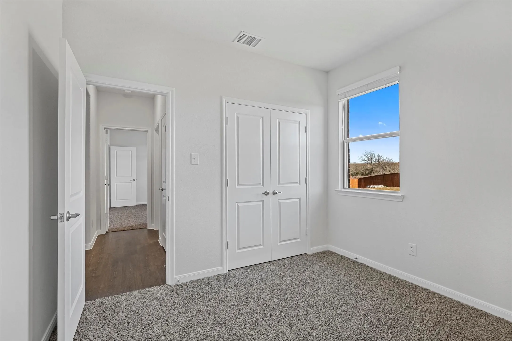 Neutral wall color, carpeted flooring, double-door closet, hallway access, and a single window