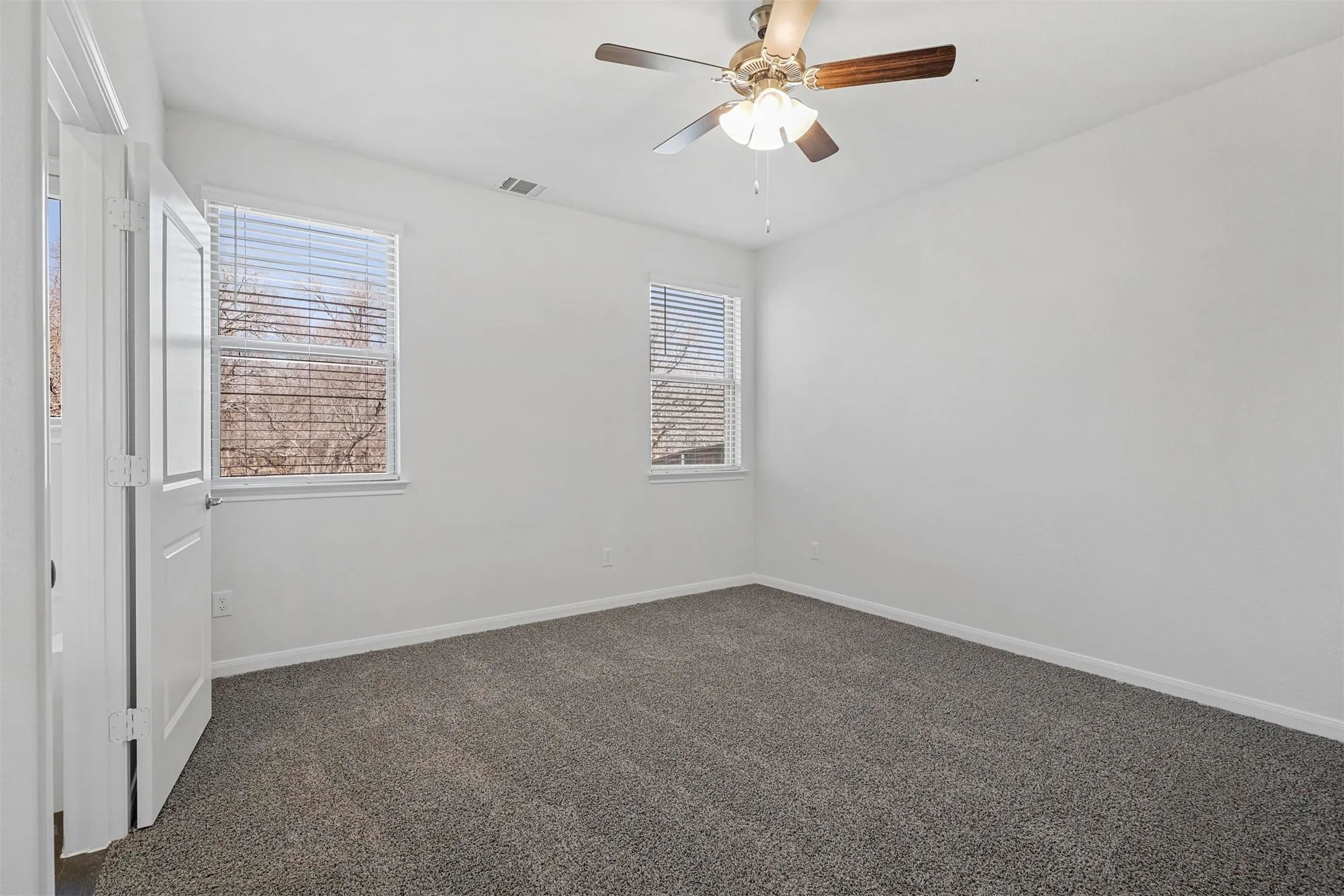 Recessed lighting, wood-finish ceiling fan, two windows with blinds, white paneled door, and gray carpeting