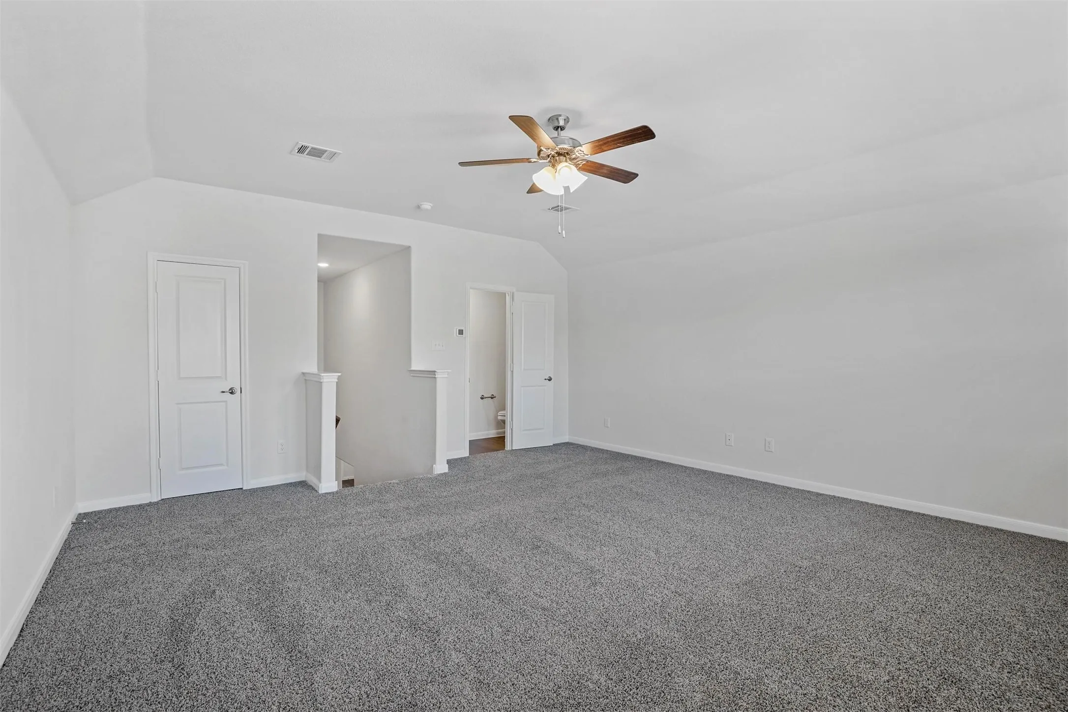 Spacious room with sloped ceilings, gray carpeting, a ceiling fan with light, and white paneled doors