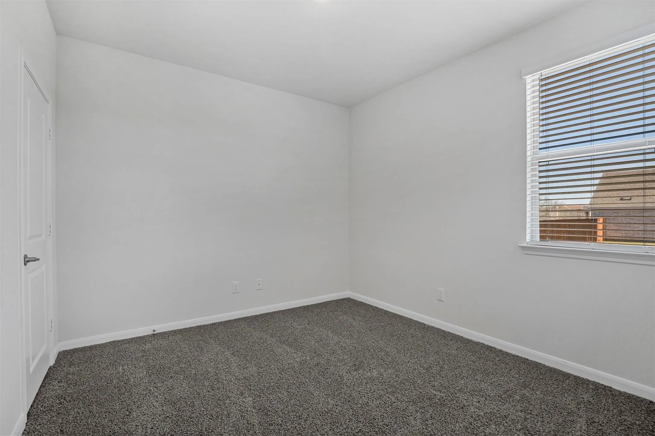 Neutral wall paint, carpet flooring, window with blinds, and white interior door
