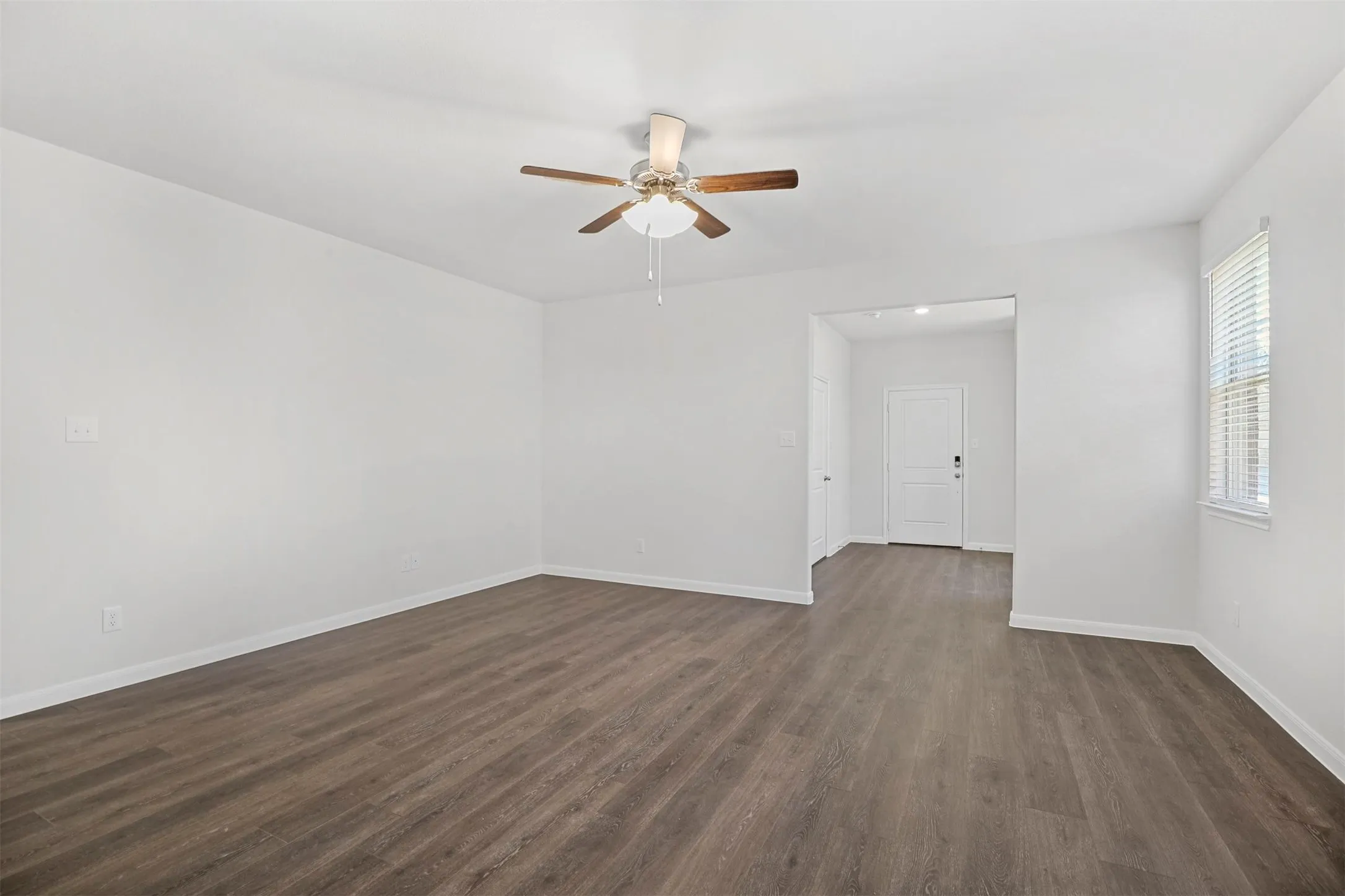 Spacious room with wood-finish flooring, white walls, and a ceiling fan