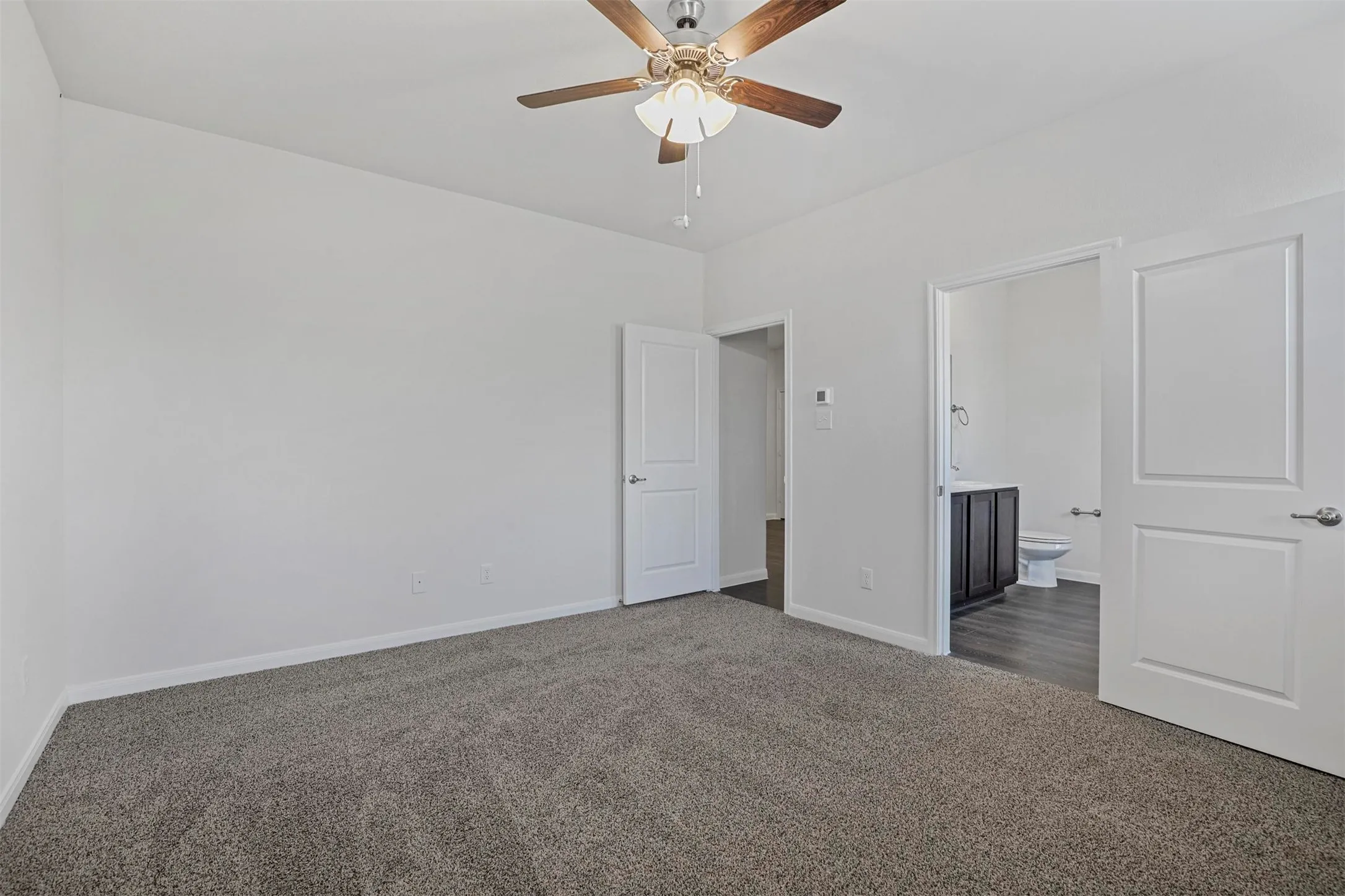 Gray carpet flooring, white walls, ceiling fan, white interior doors, dark wood-finish vanity