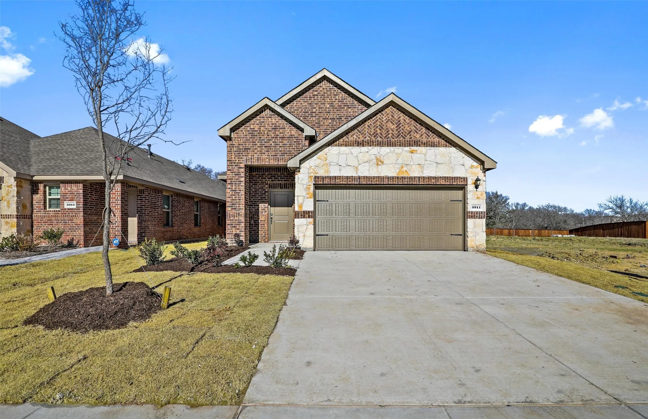 Brick and stone exterior with a two-car garage, concrete driveway, and landscaped front yard