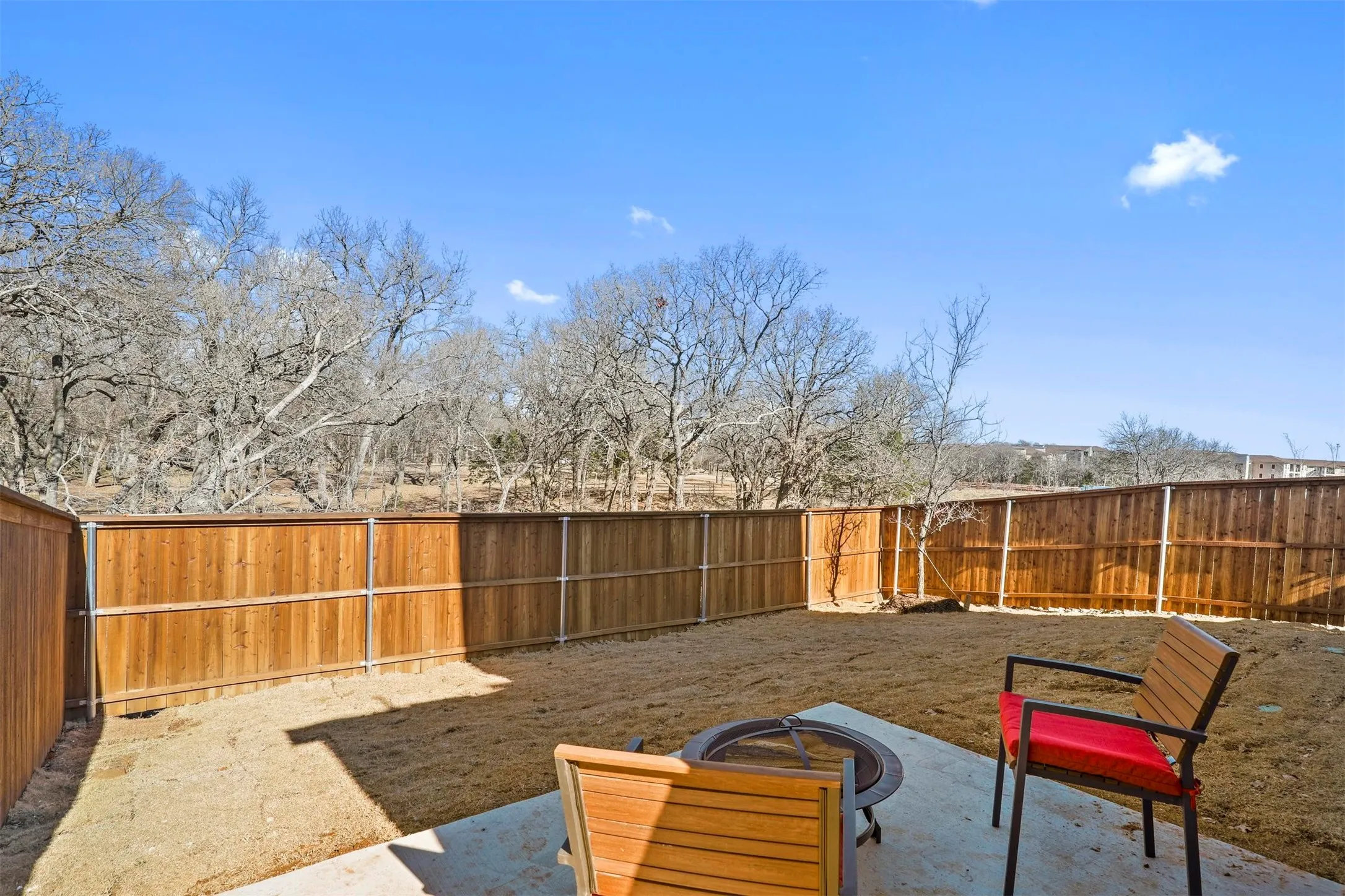 Private backyard with a wood privacy fence, concrete patio, and a natural landscape beyond