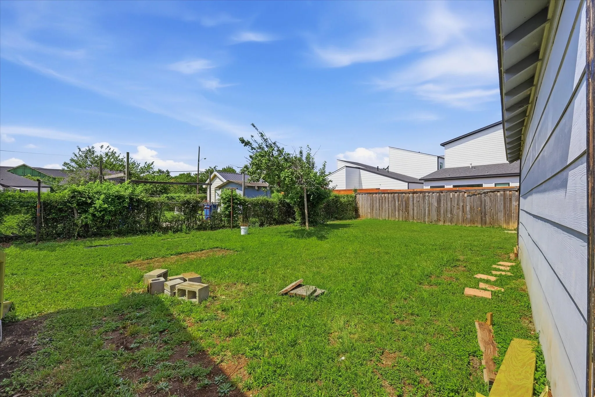 Backyard view featuring the detached garage, open lawn, rear ramp access, and mature greenery. This angle captures the property’s outdoor potential, offering generous space for pets, play, gardening, seating areas, or future landscaping enhancements in a private fenced setting.