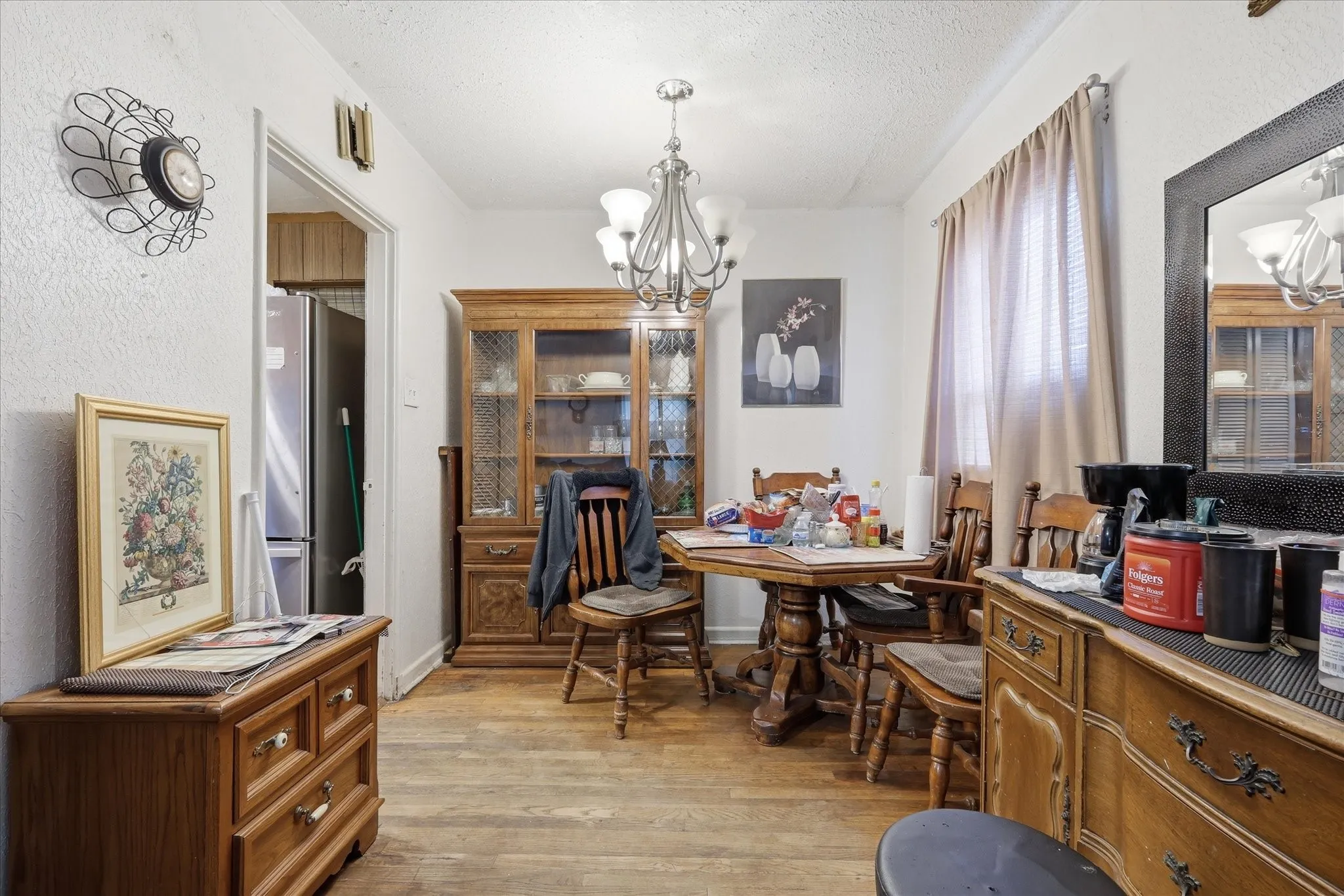 Dining area with wood-look flooring, white walls, chandelier lighting, and a convenient opening into the kitchen. The space offers room for a dining table, china cabinet, buffet, or additional storage, making it practical for meals, entertaining, or flexible daily use. Natural light from the window softens the room, while the nearby kitchen access keeps the layout functional.