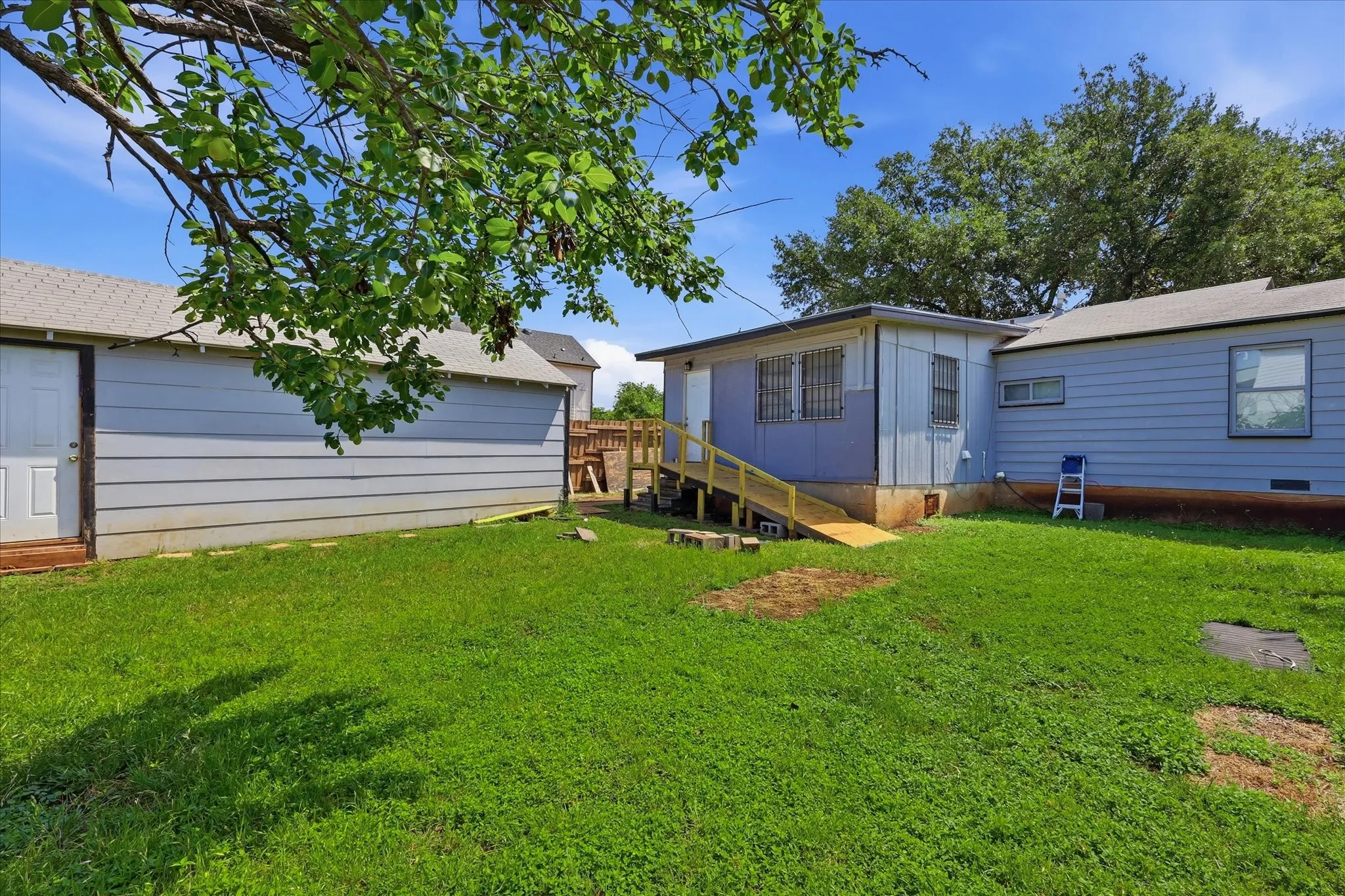 Wide rear yard view with the detached garage, ramped rear access, and open green space all visible. The layout creates a highly usable backyard with room to relax, entertain, plant a garden, or design a customized outdoor retreat while maintaining practical access to the home and garage.