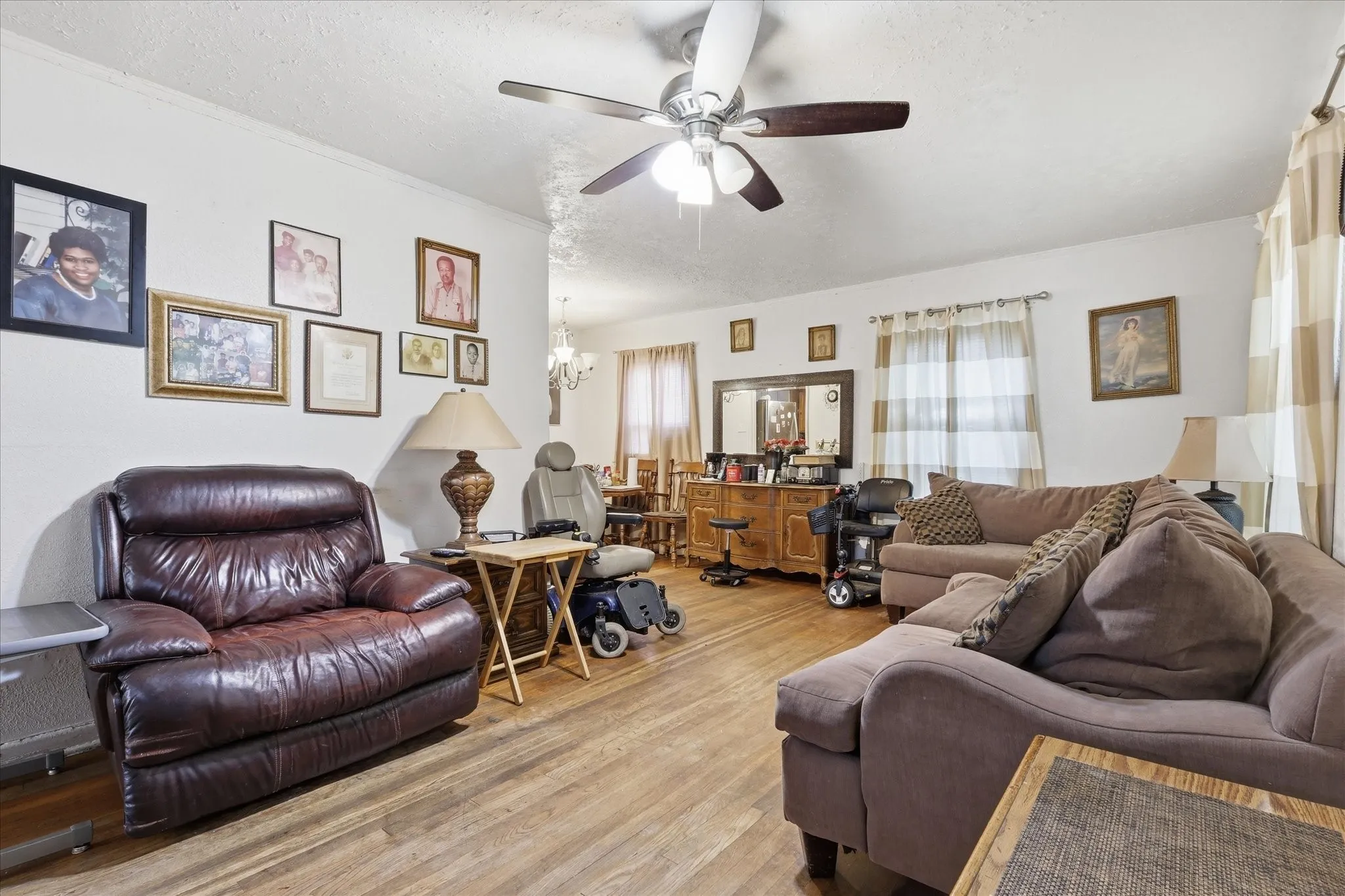 Spacious living room with wood-look flooring, white walls, ceiling fan, and multiple windows that bring in natural light. The room offers generous seating space and an easy flow toward the dining area, creating a comfortable setting for relaxing, hosting, or everyday living. Its open feel and flexible wall space allow buyers to imagine a variety of furniture arrangements.