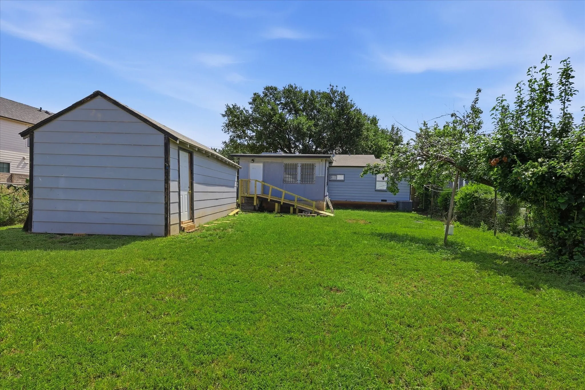 Wide backyard perspective highlighting the open grassy lawn, detached garage, rear exterior, and fenced perimeter. The yard offers an impressive amount of usable outdoor space with room for seating, recreation, gardening, or additional landscaping. This view helps capture the scale of the lot and the lifestyle potential available beyond the home itself.