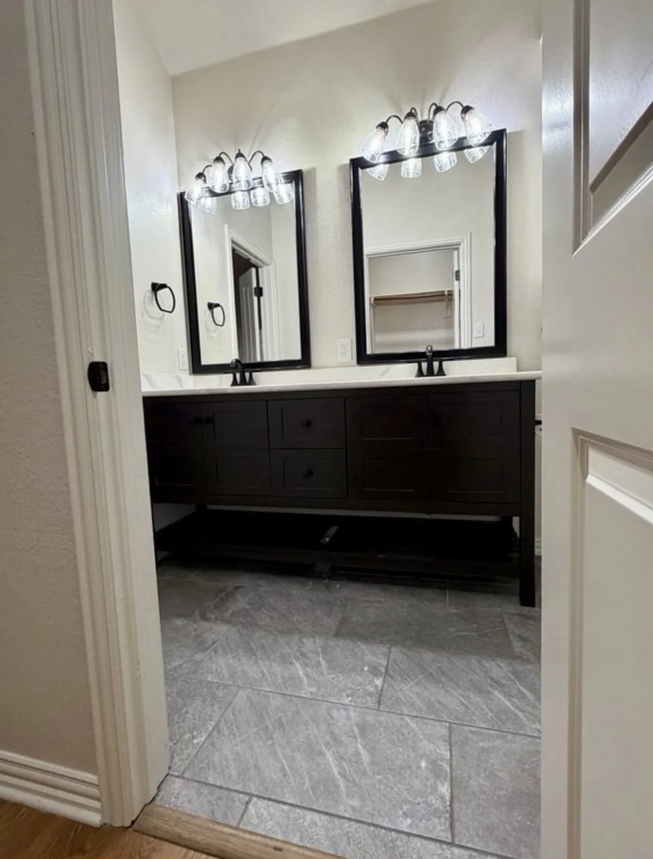 Dual vanity with dark wood cabinetry, white countertops, black-framed mirrors, and matching black fixtures