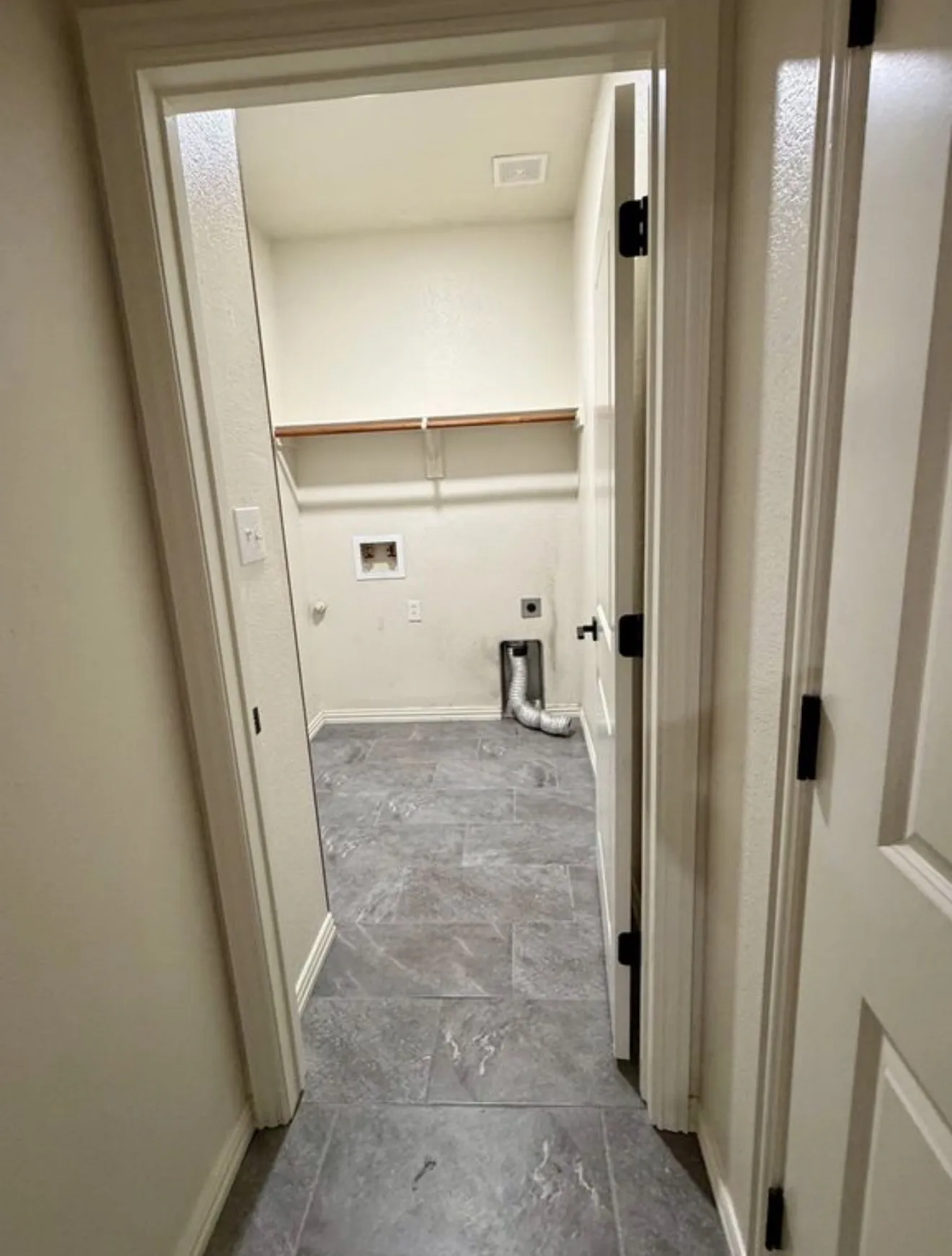 Dedicated utility space featuring durable tile flooring, wood shelving, and essential appliance hookups