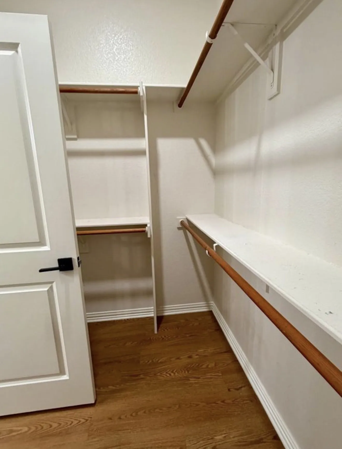 Walk-in closet featuring wood-finish flooring, white shelving, and hanging rods
