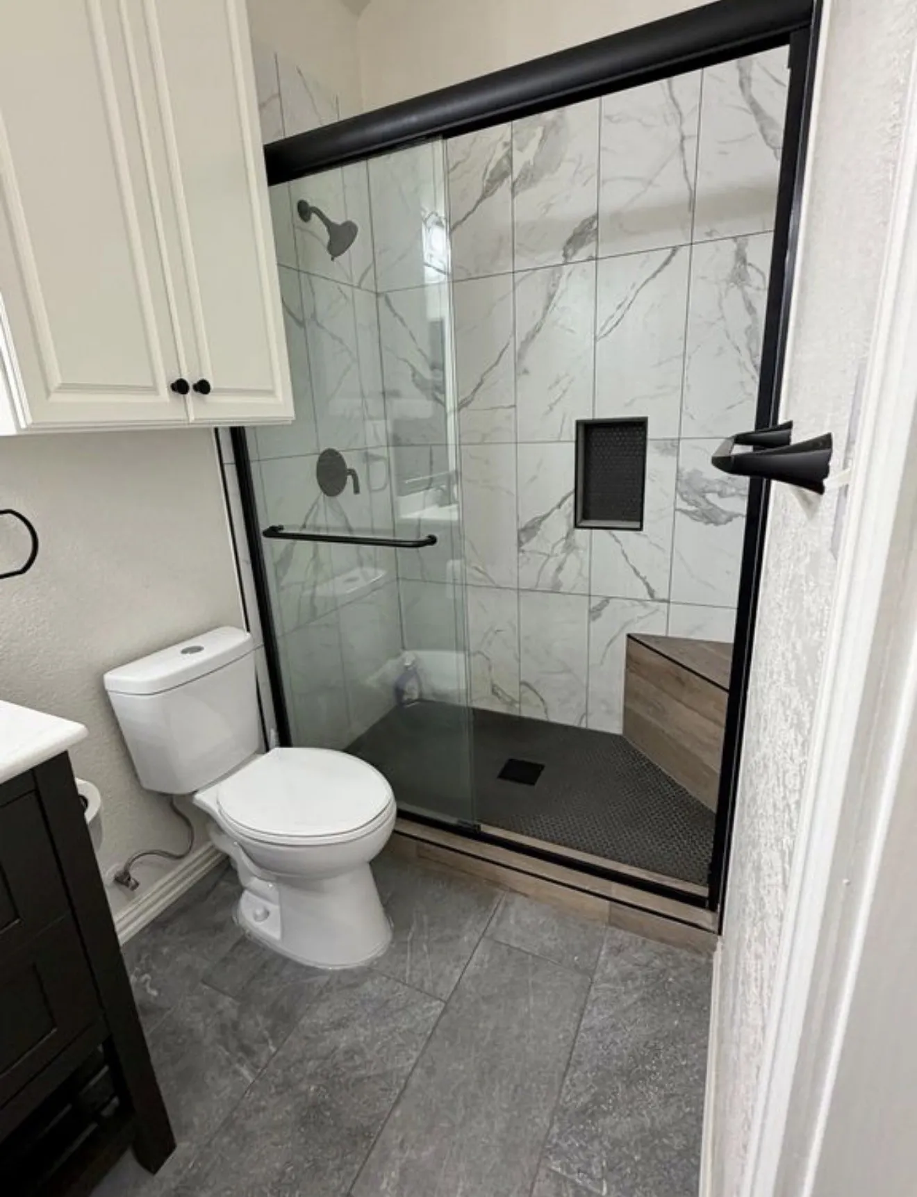Modern primary bathroom featuring a frameless glass shower enclosure with matte black hardware and fixtures, marble-look tile surround, a linear floor drain, and a separate toilet with white porcelain finish