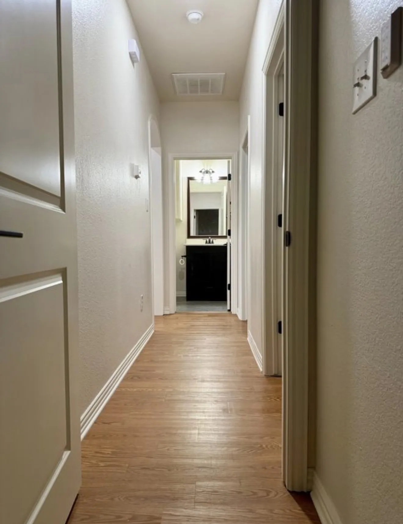 Wood-finish flooring extending through a neutral-toned hallway with an arched doorway