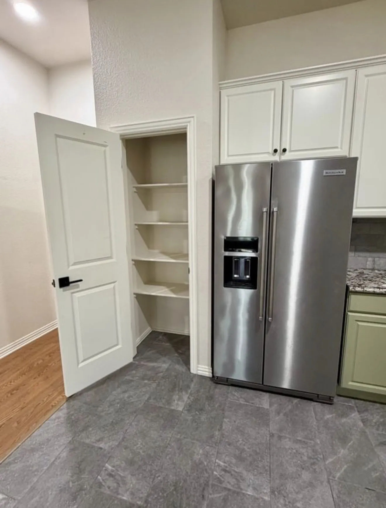 Stainless steel refrigerator, white upper cabinetry, green lower cabinetry, granite-finish countertop, and gray tile flooring