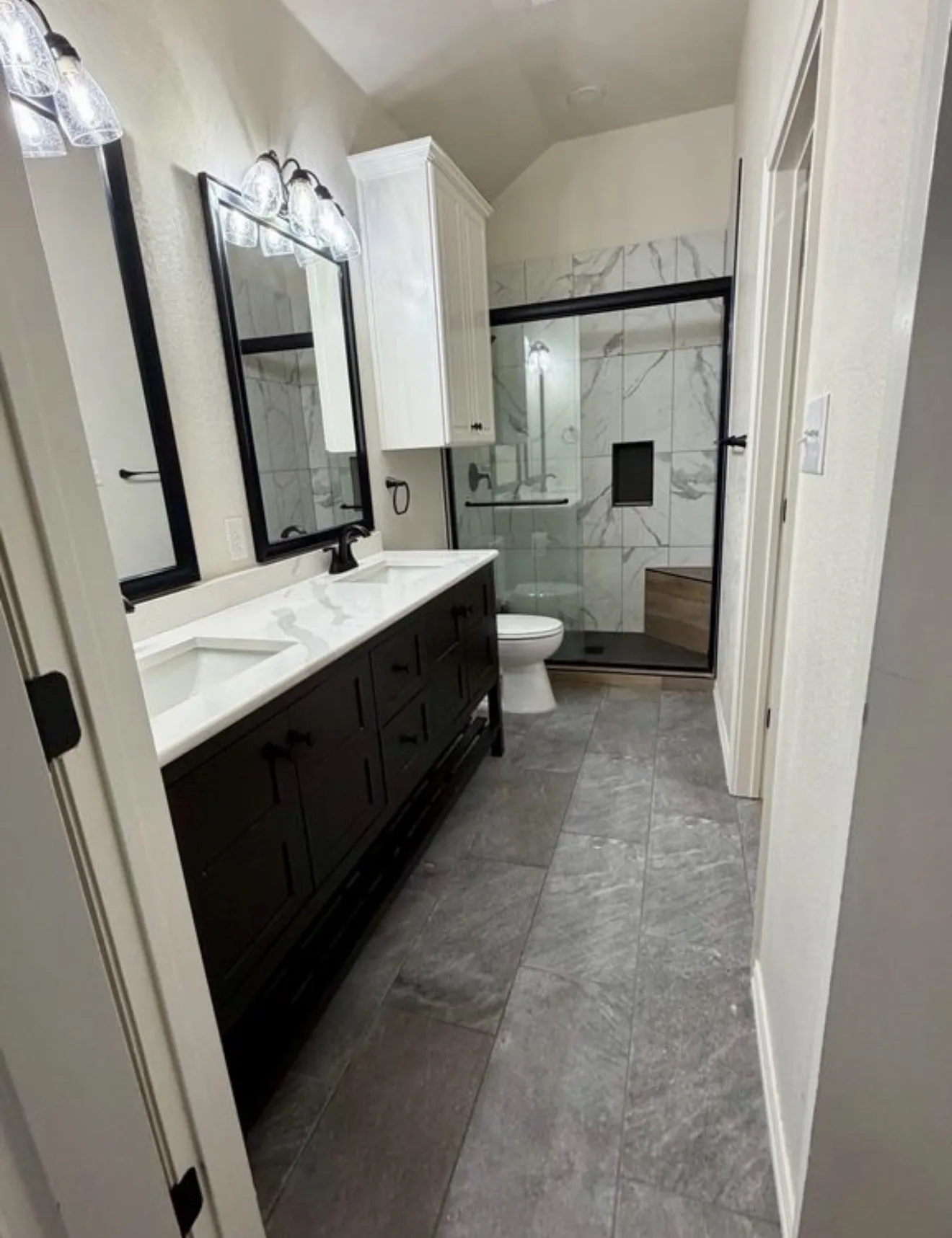 Primary bathroom featuring dual vanities with white quartz countertops, black cabinetry with integrated hardware, framed mirrors with black trim, and ceramic tile flooring