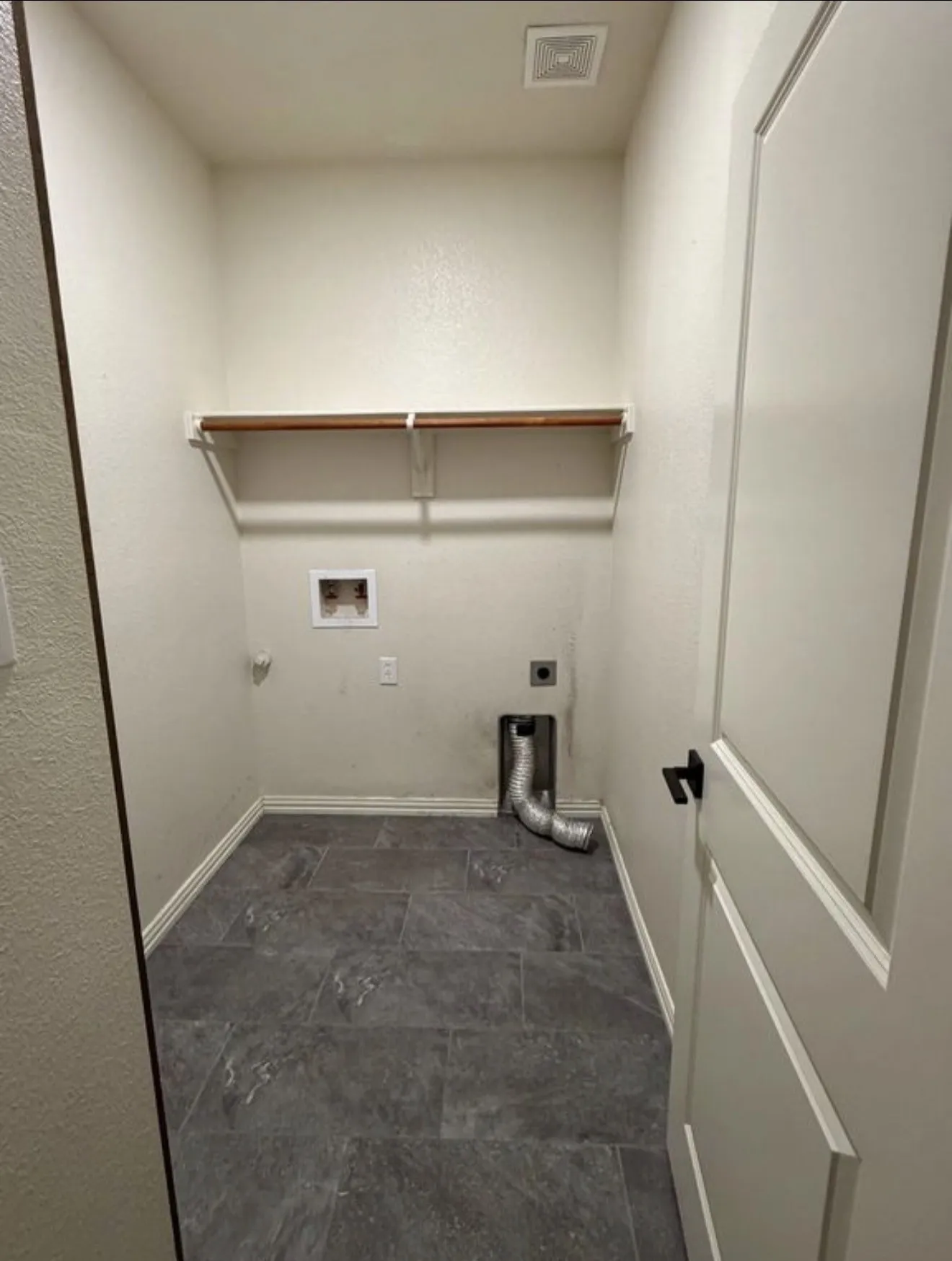 Laundry area featuring tiled flooring, a built-in wood-finish shelf, and a panel-style door with matte black hardware