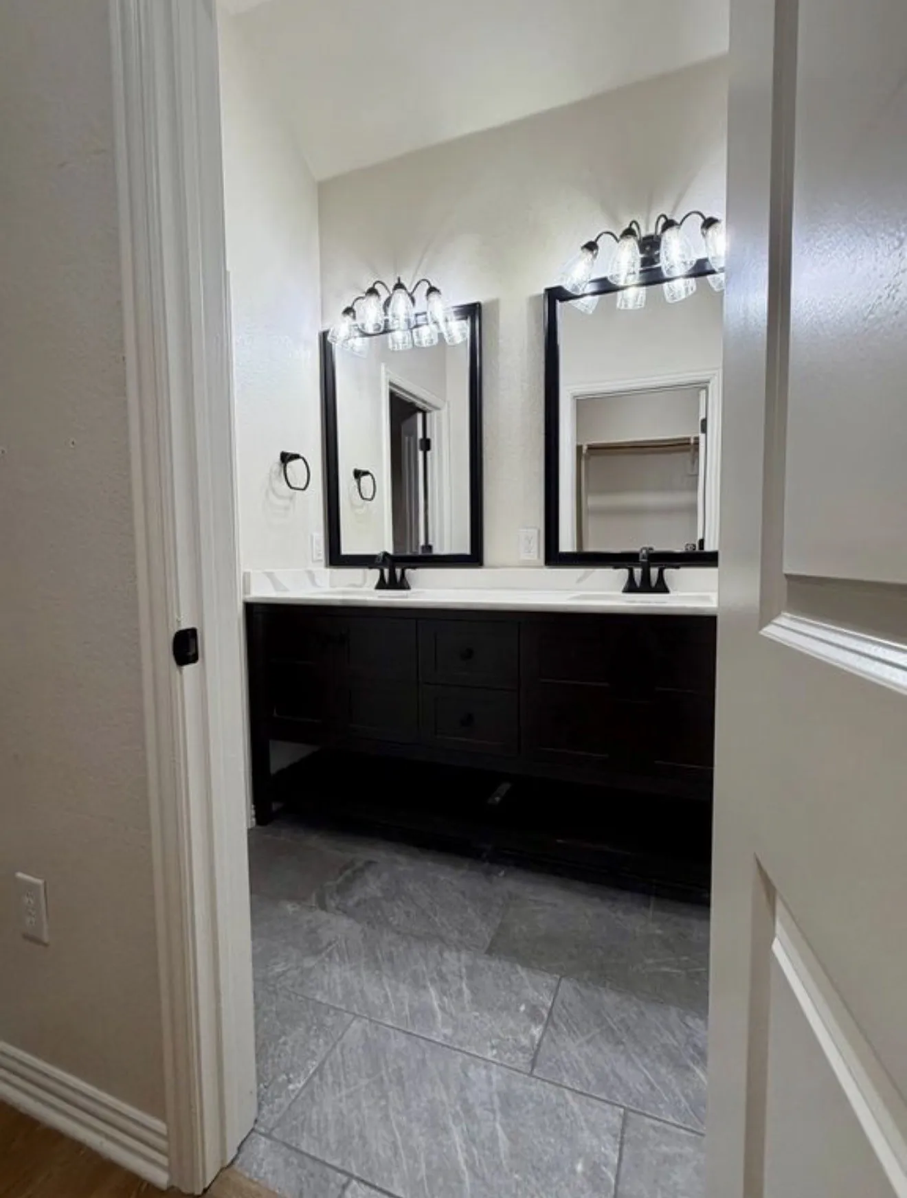 Double vanity with dark wood-finish cabinetry, white countertops, and dual framed mirrors